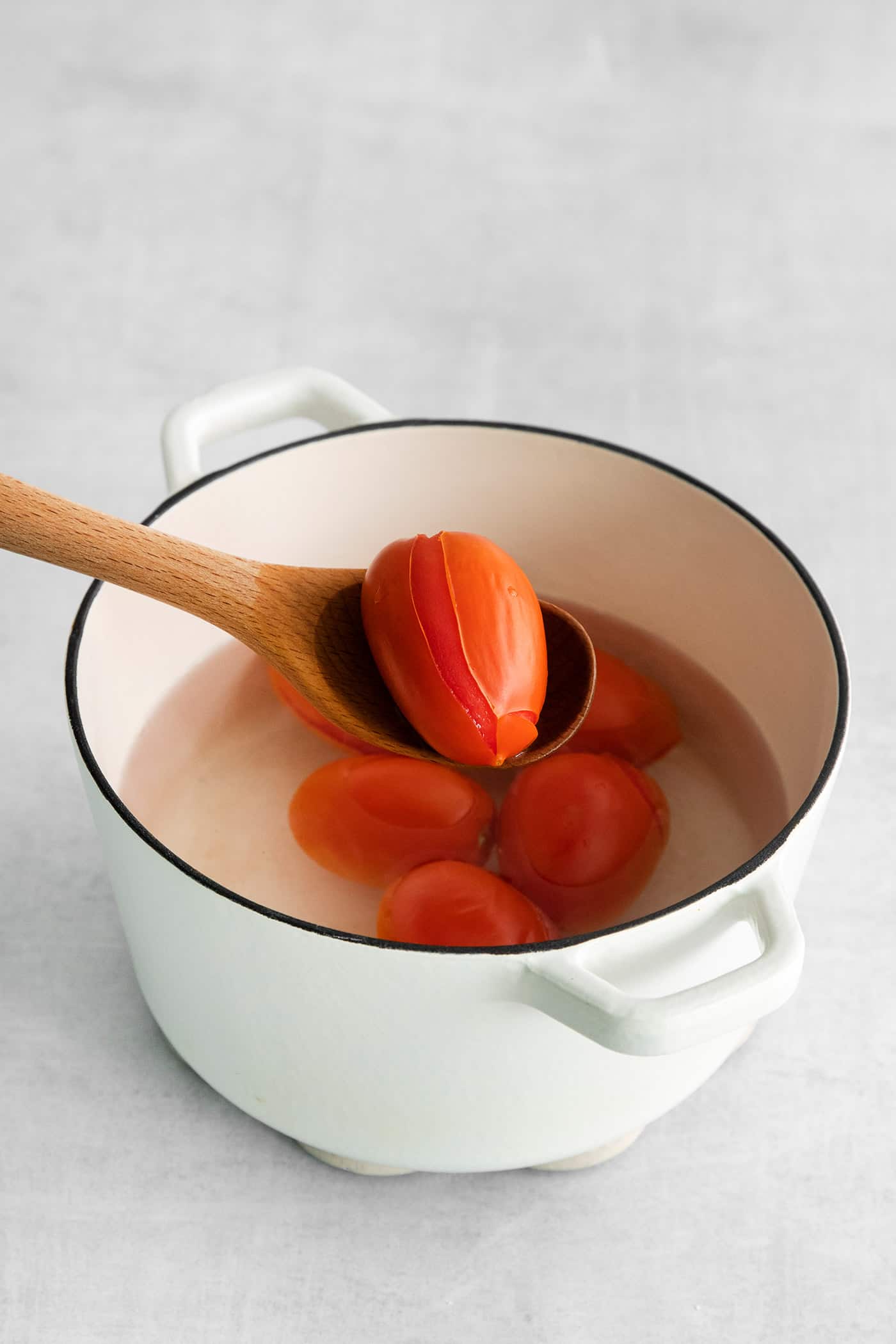 A spoon pulling a roma tomato from a pot of water