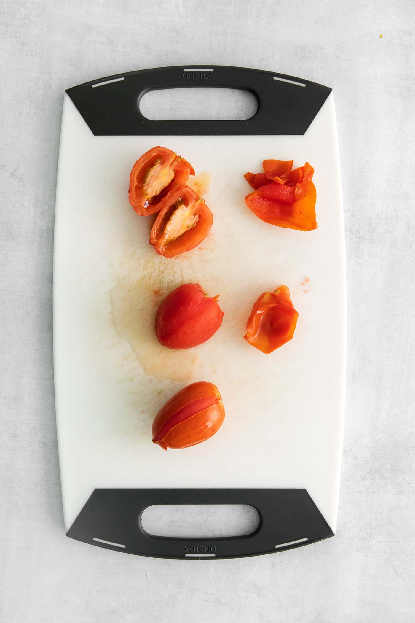 Skinned tomatoes and tomatoes cut in half on a cutting board