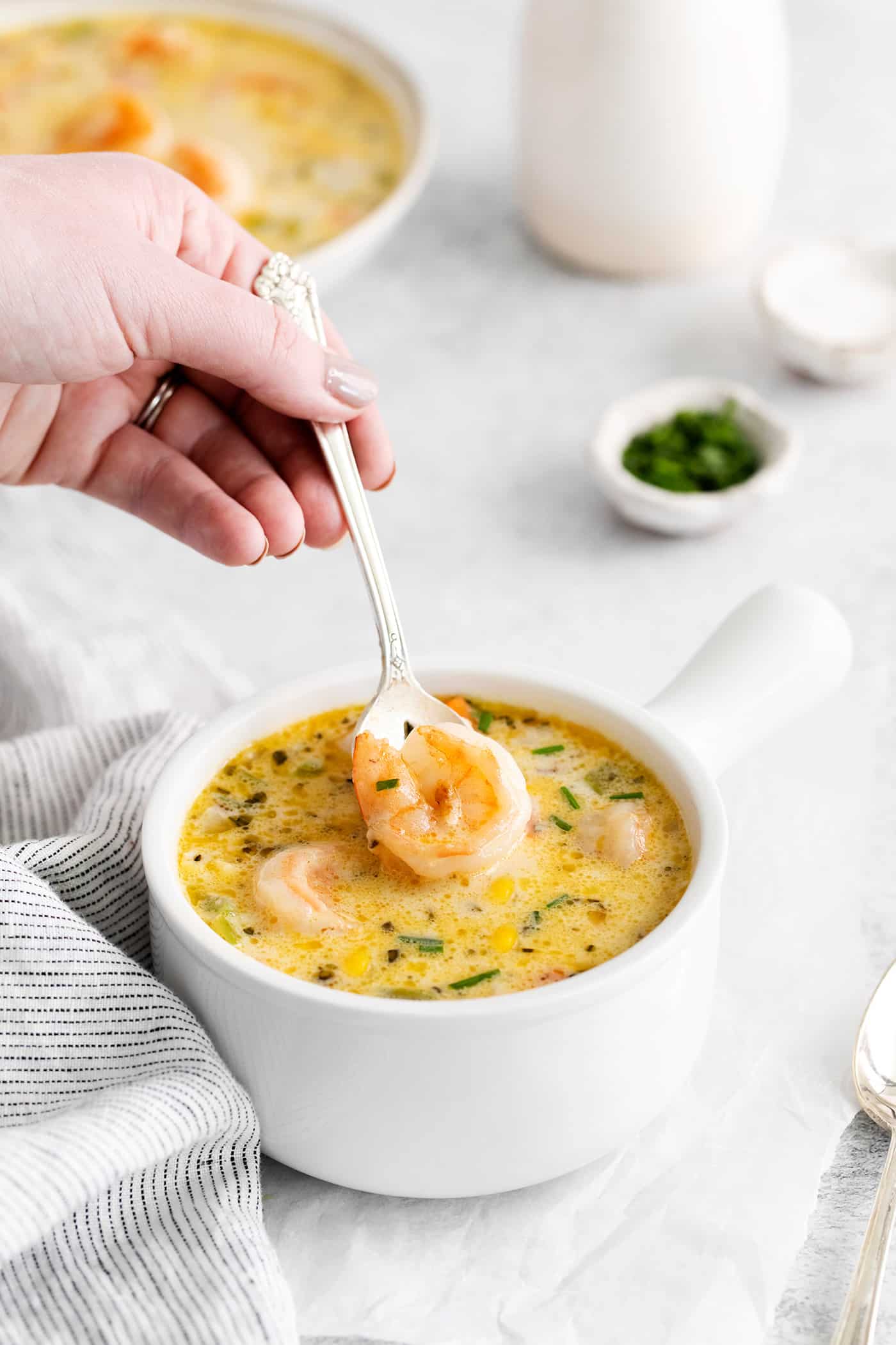 A spoon lifting a shrimp from a bowl of shrimp corn chowder