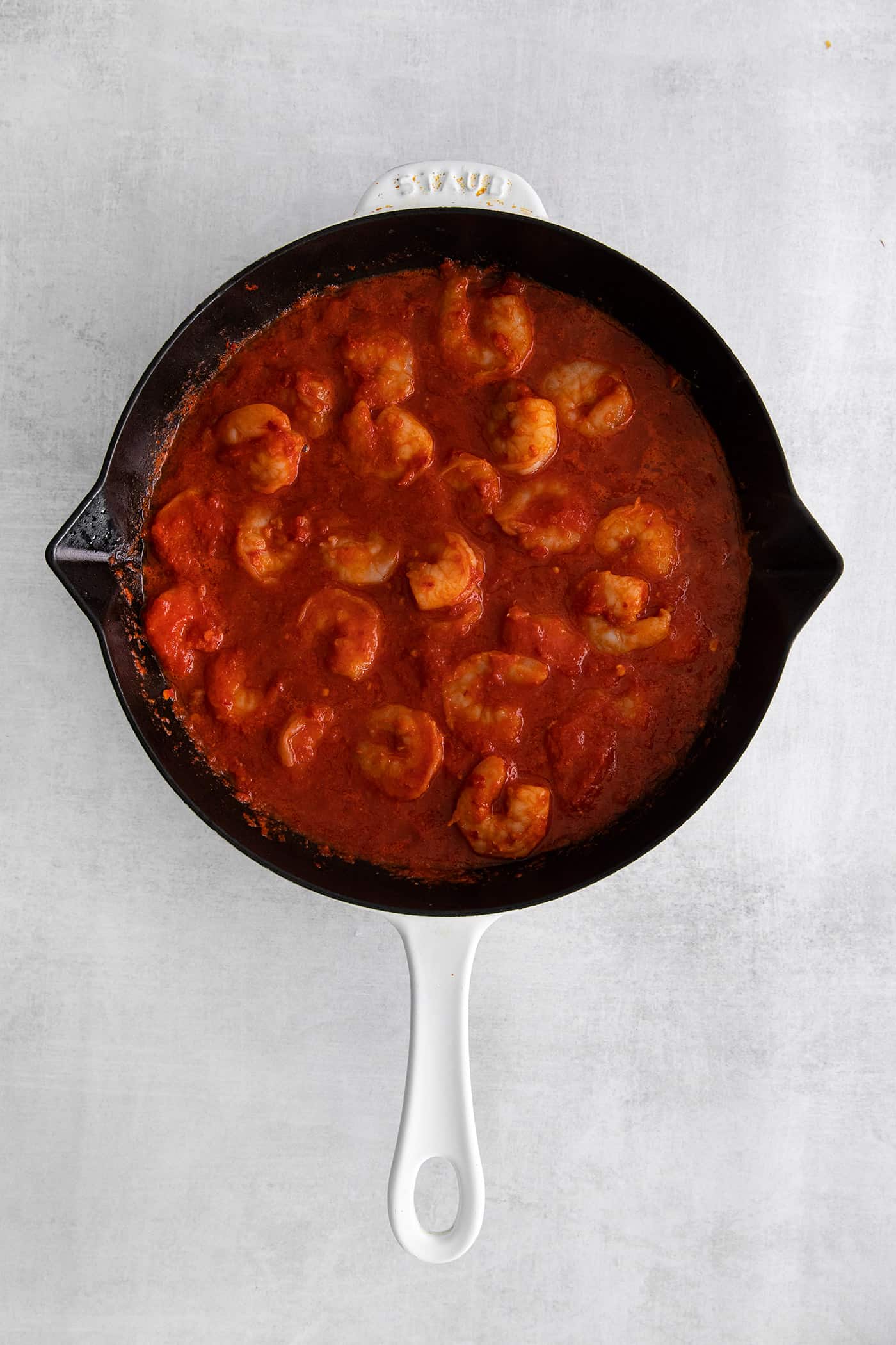 Overhead view of shrimp in a cast iron skillet with red sauce