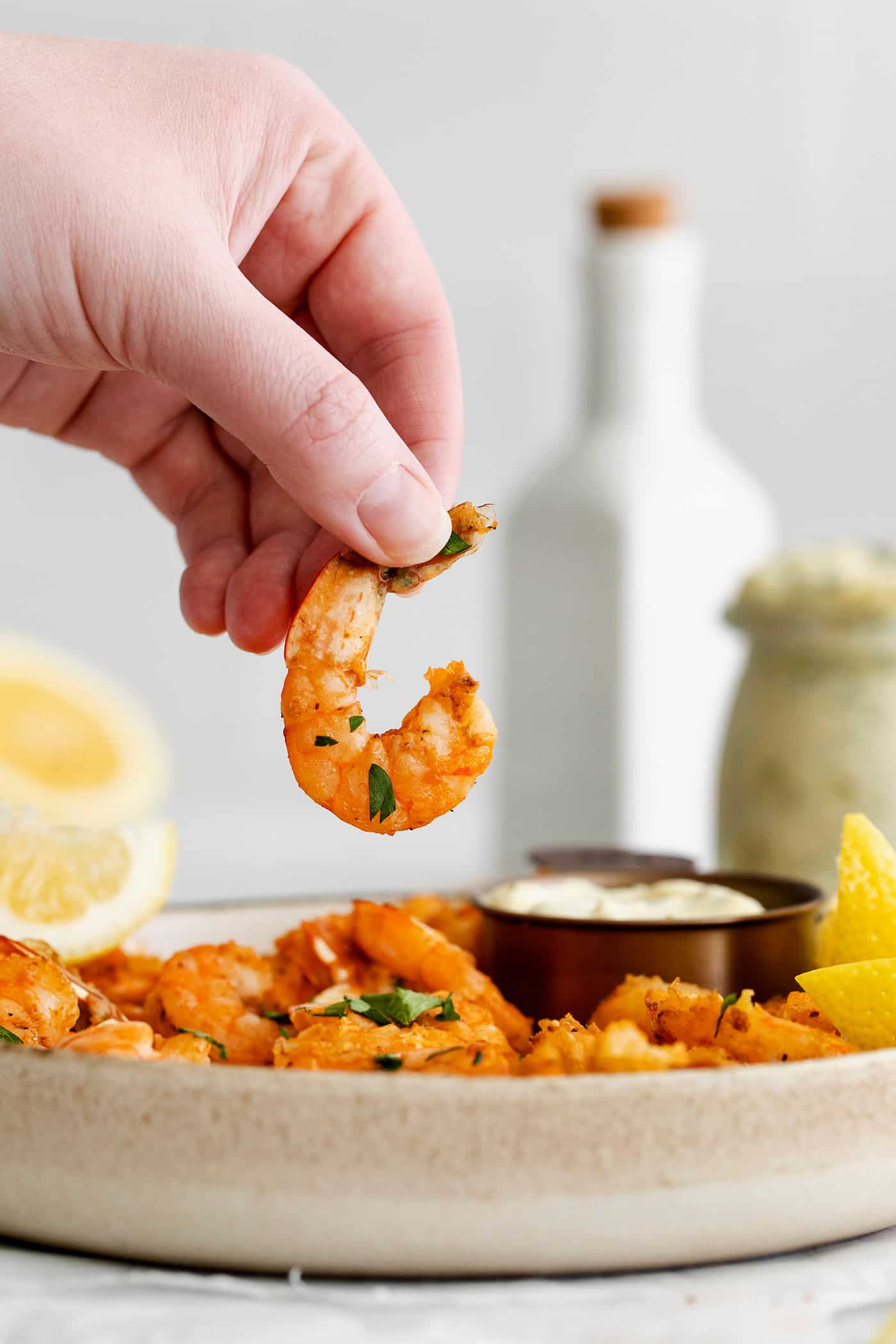 A hand holding seasoned shrimp over tartar sauce.