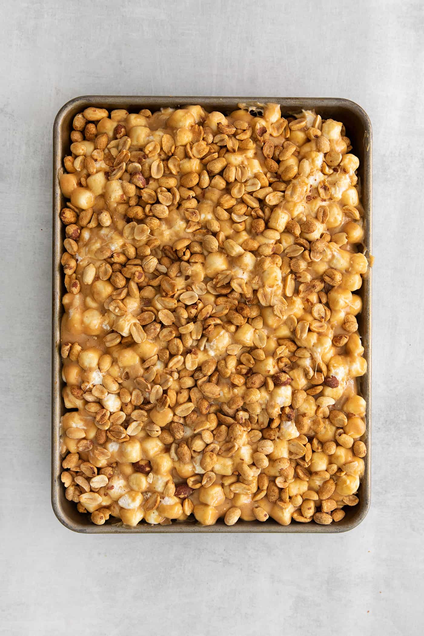 peanuts sprinkled over the top of the salted nut roll bars in a rimmed pan