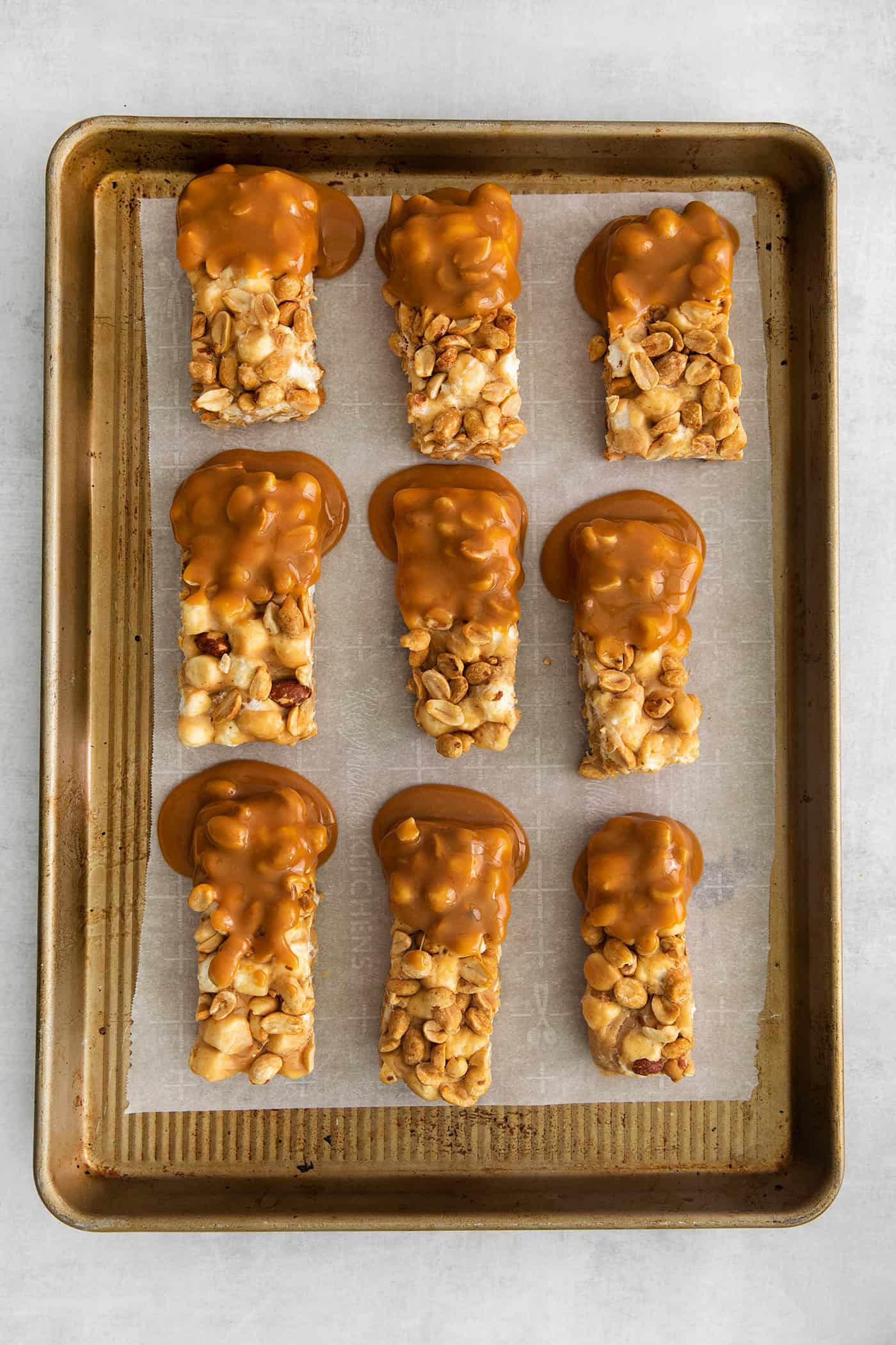 salted nut roll bars dipped in caramel, on parchment paper in a rimmed pan