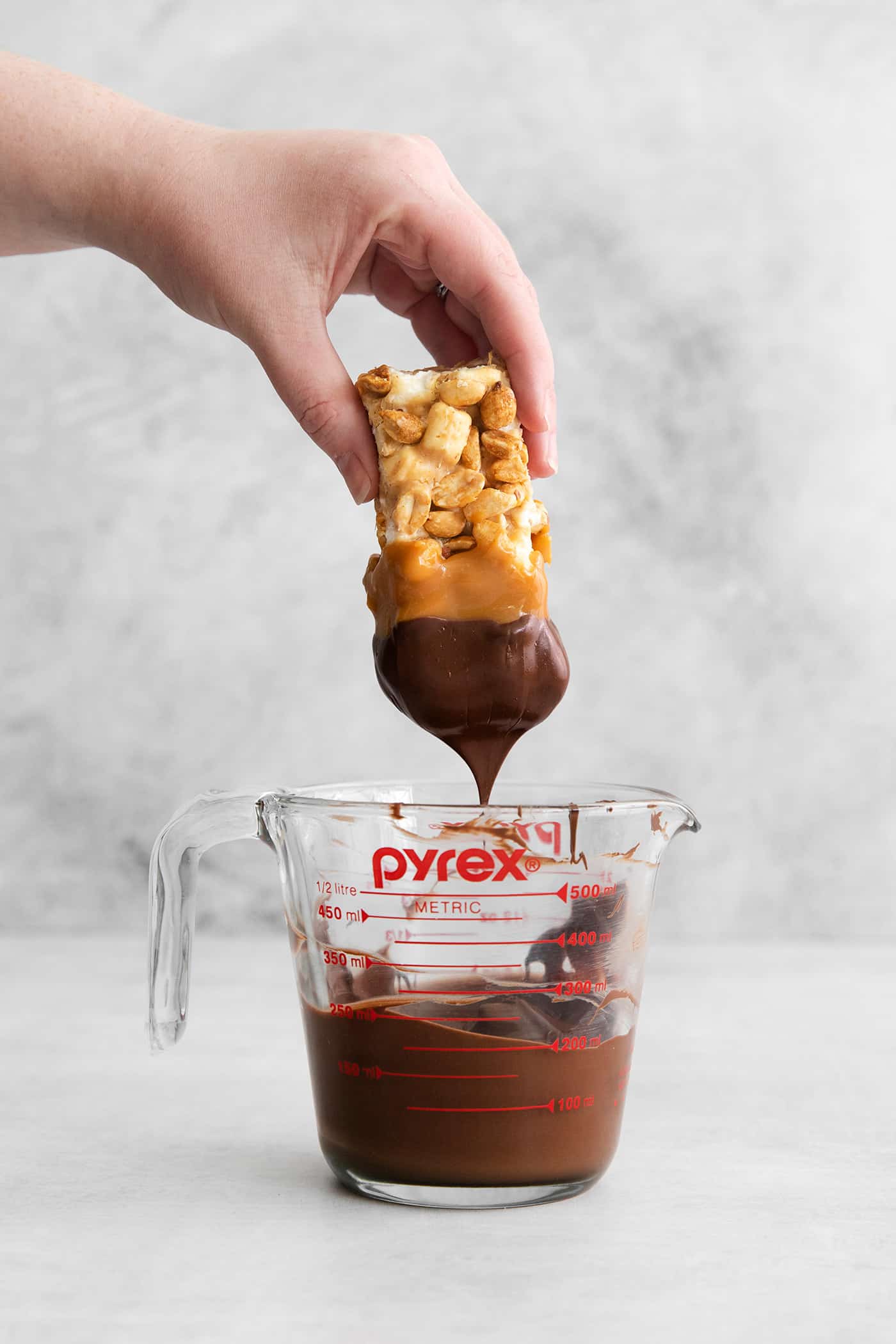 a hand dipping a salted nut roll bar into melted chocolate