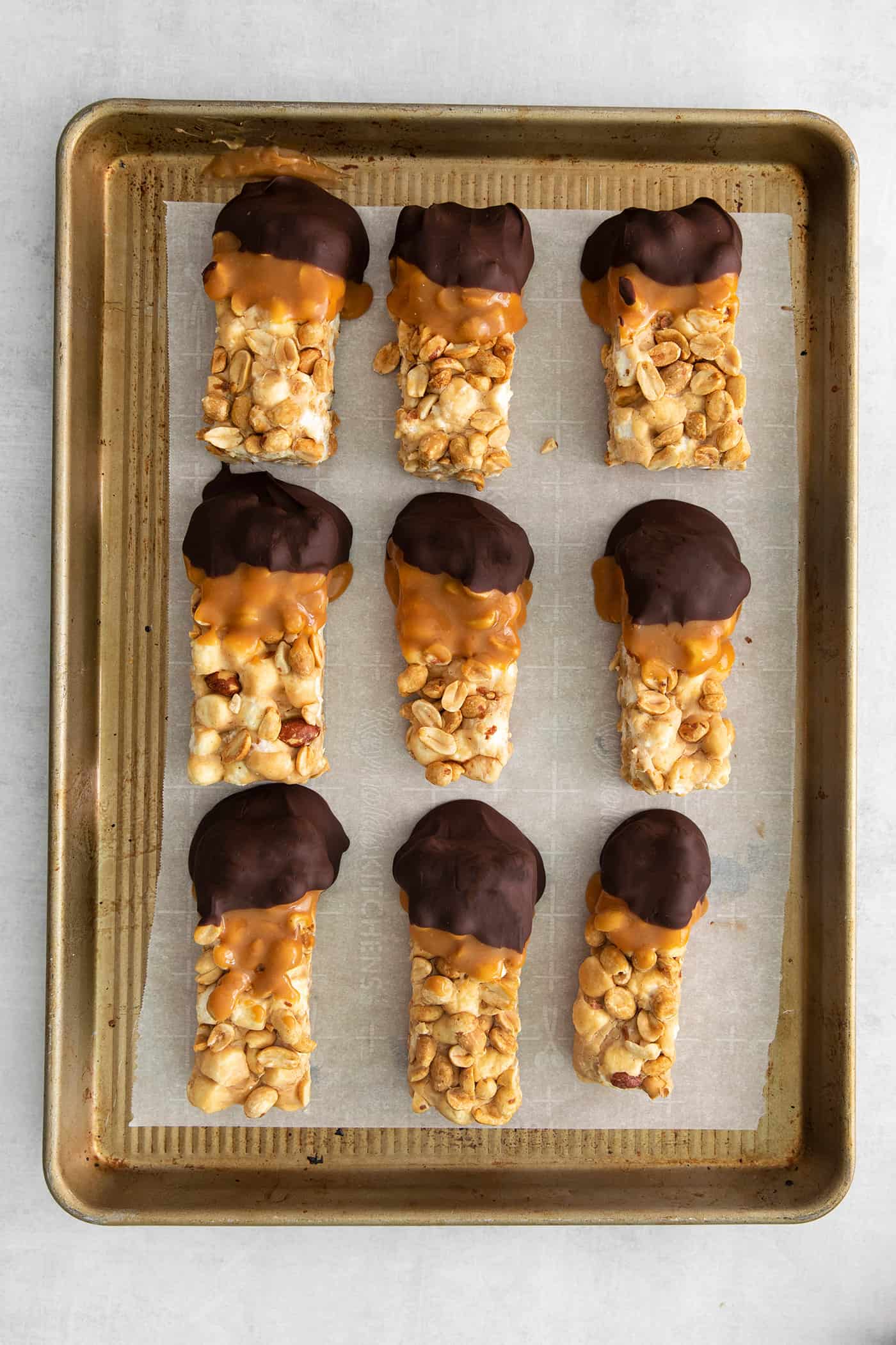 salted nut roll bars dipped in caramel and chocolate, on parchment paper in a rimmed pan