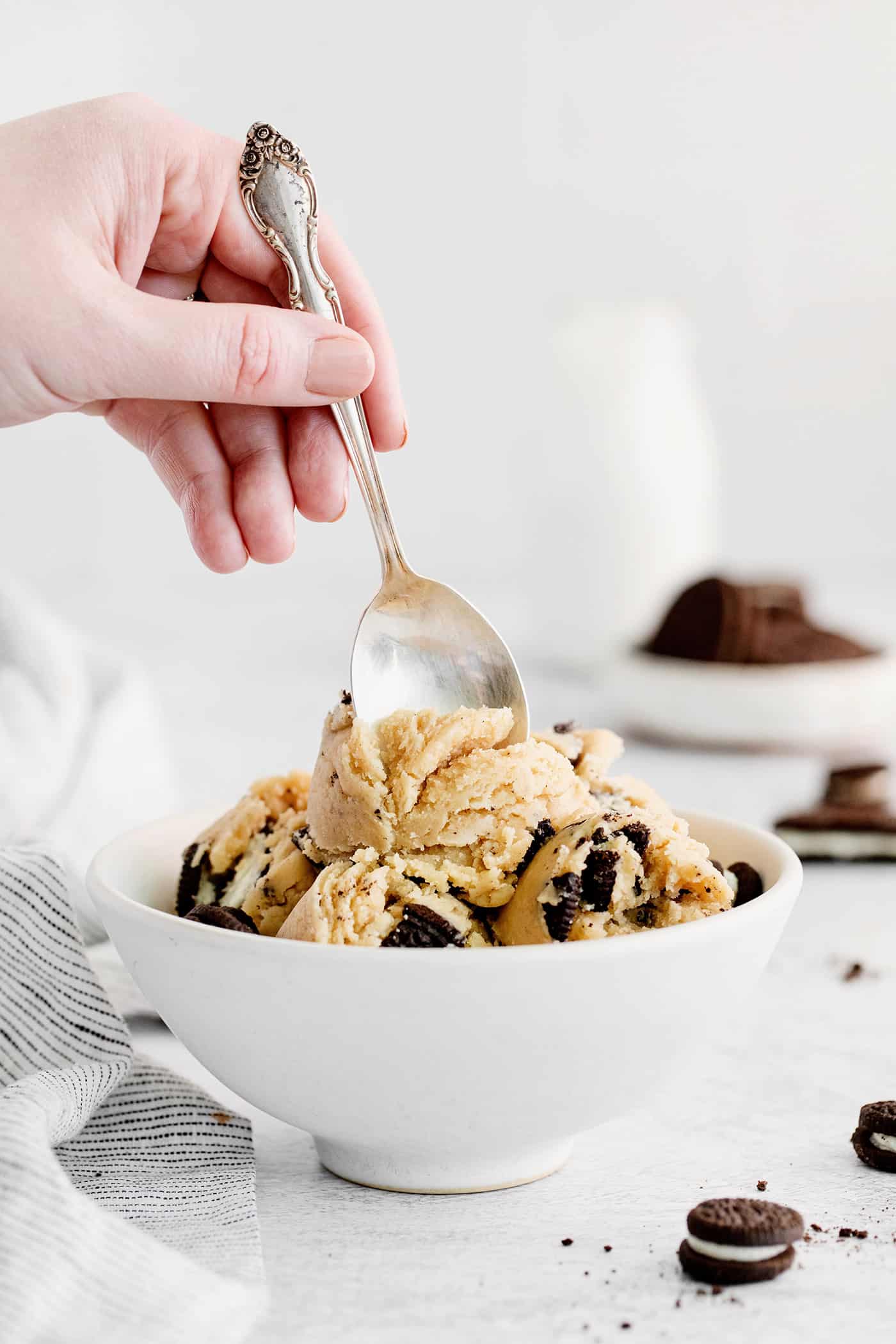 A spoon digging in to edible cookie dough in a white bowl