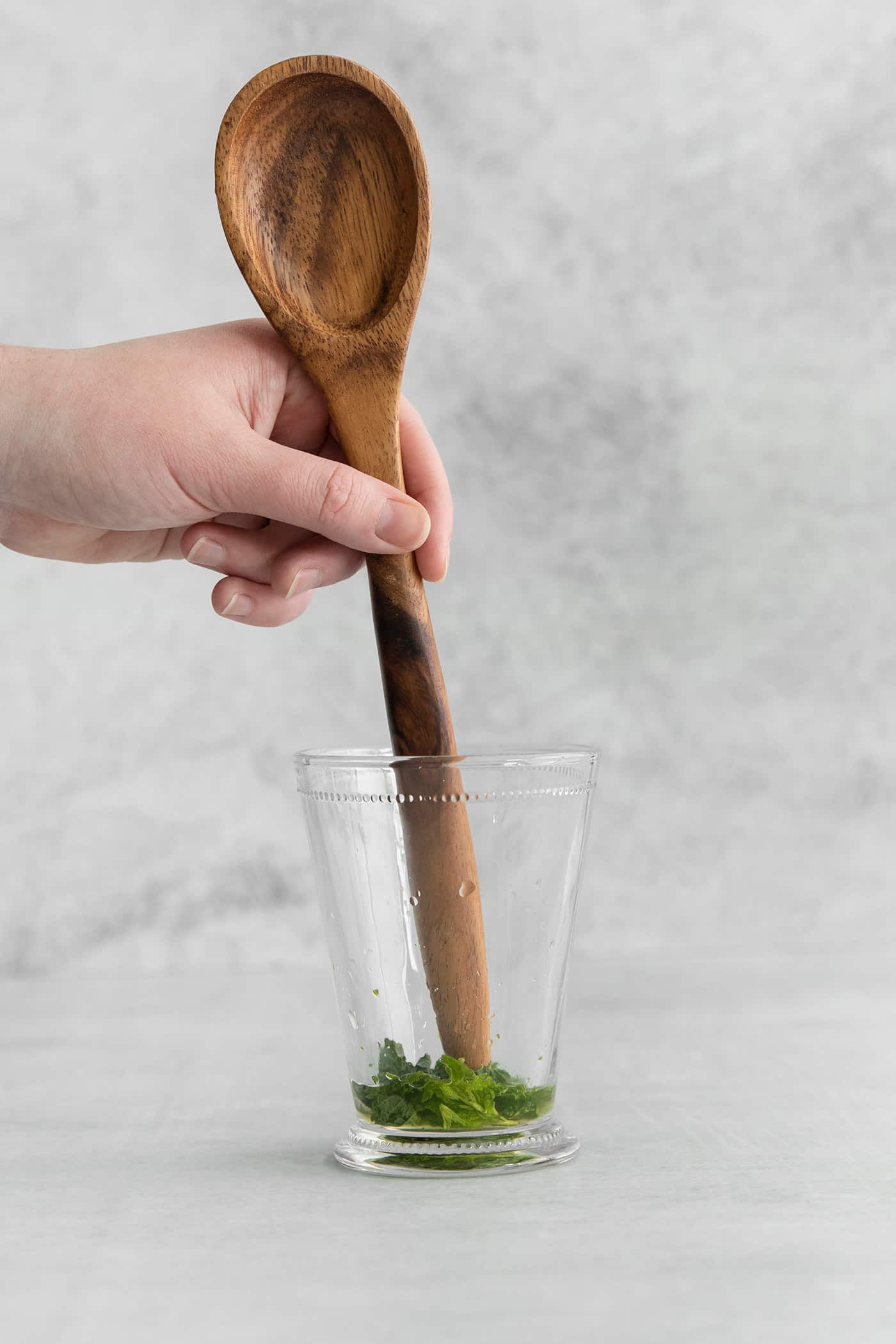 The end of a wooden spoon muddling mint in a glass