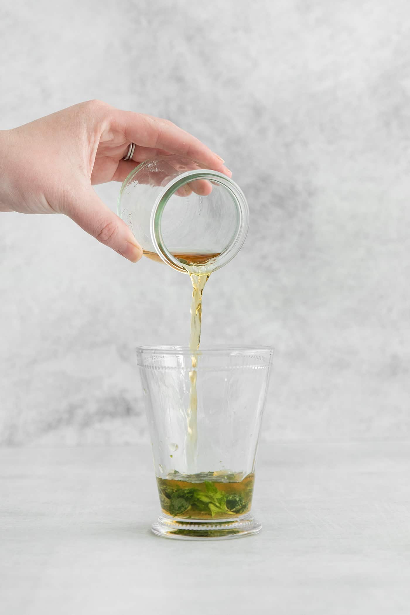 Bourbon being poured into a glass over muddled mint