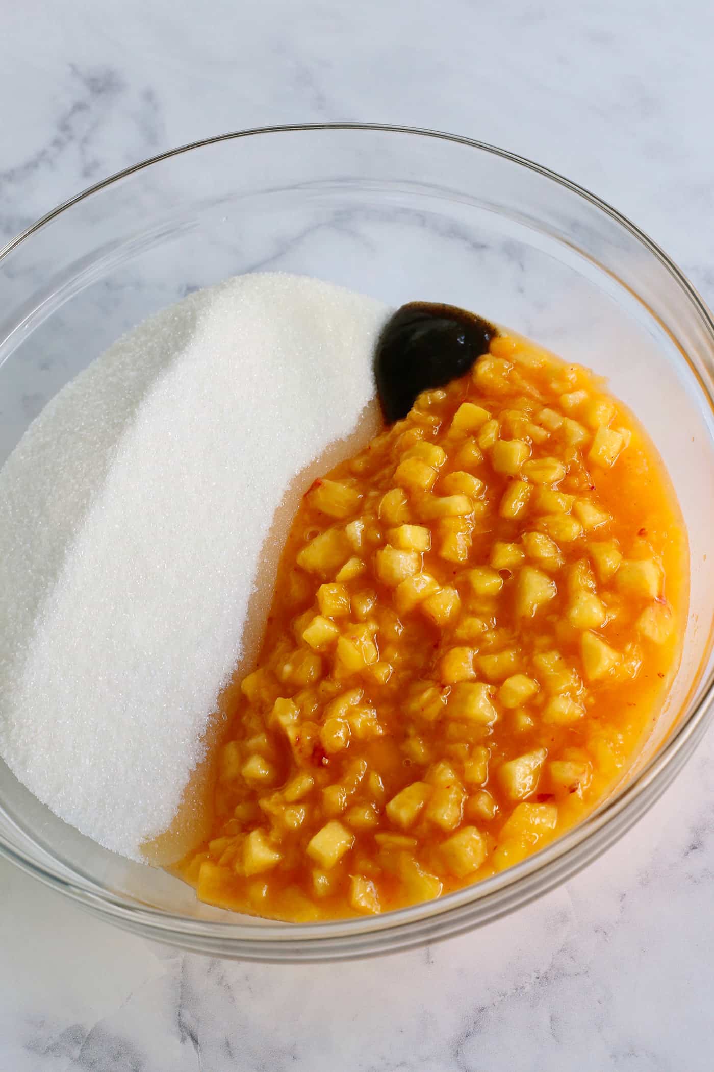 peaches, sugar, and vanilla bean paste in a large clear bowl