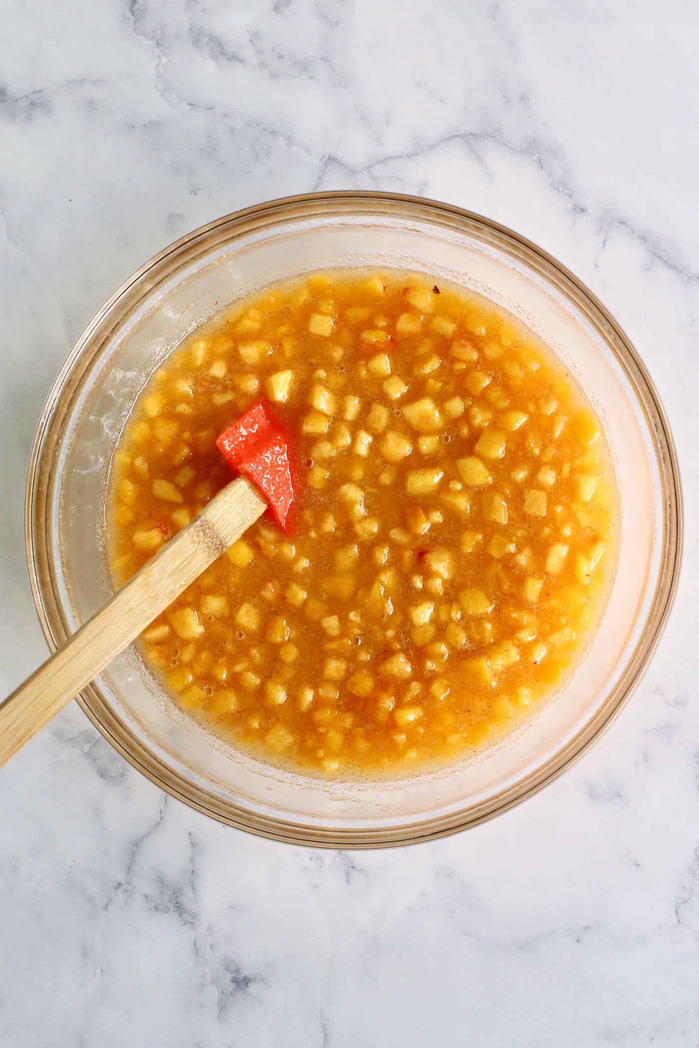 chopped and mashed peaches in a clear bowl, mixed with sugar and vanilla bean paste