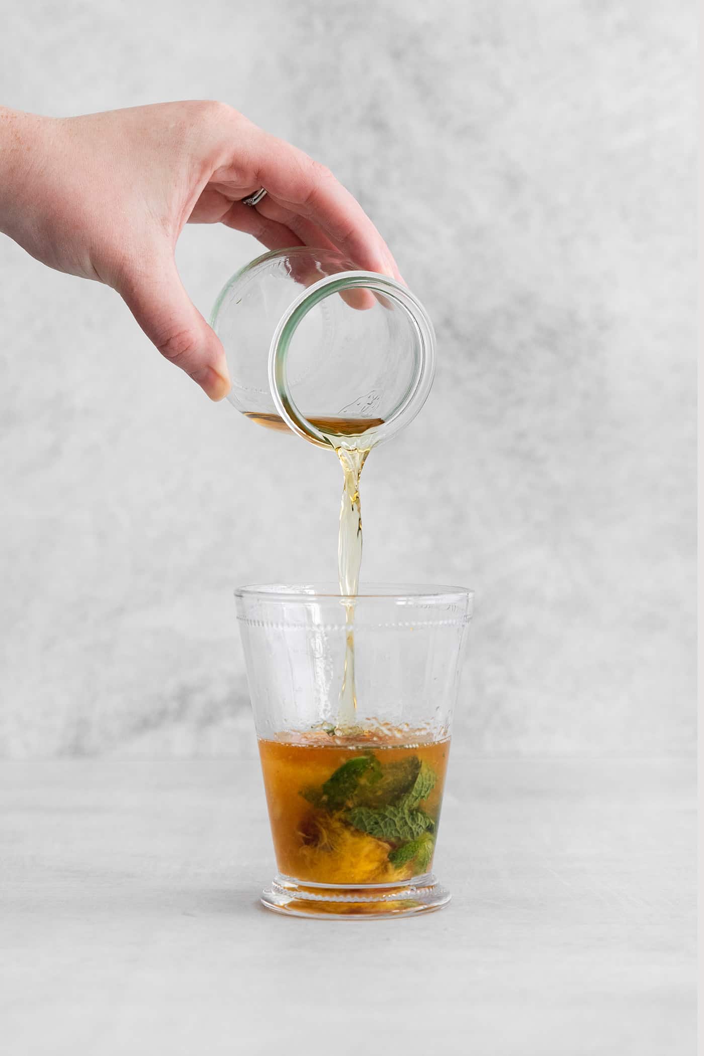 Bourbon being poured into a glass with muddled peaches and mint