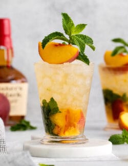 A peach julep cocktail garnished with a peach slice