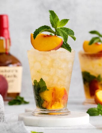 A peach julep cocktail garnished with a peach slice