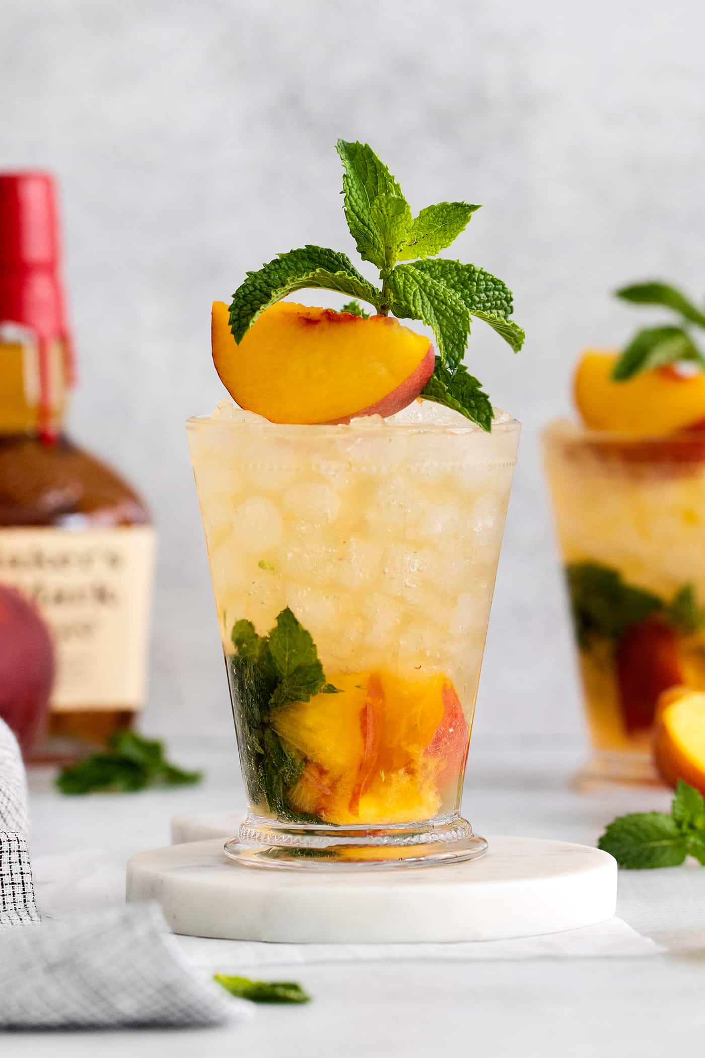 A peach julep cocktail garnished with a peach slice