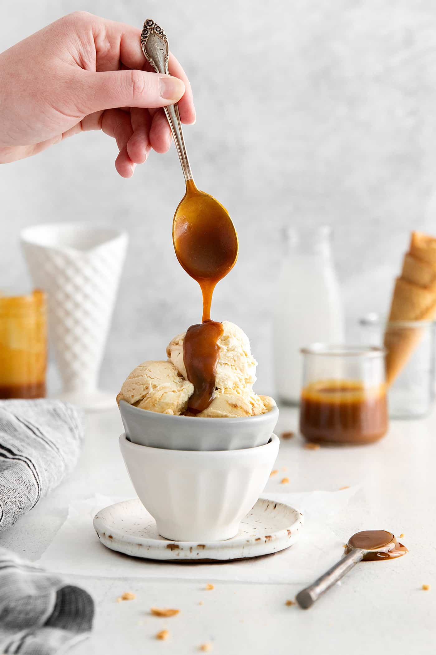 A spoon drizzling caramel sauce of a bowl of ice cream