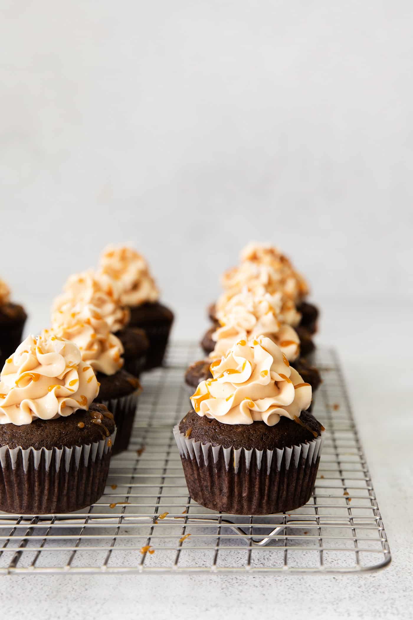 chocolate cupcakes on a cooling rack, topped with caramel frosting