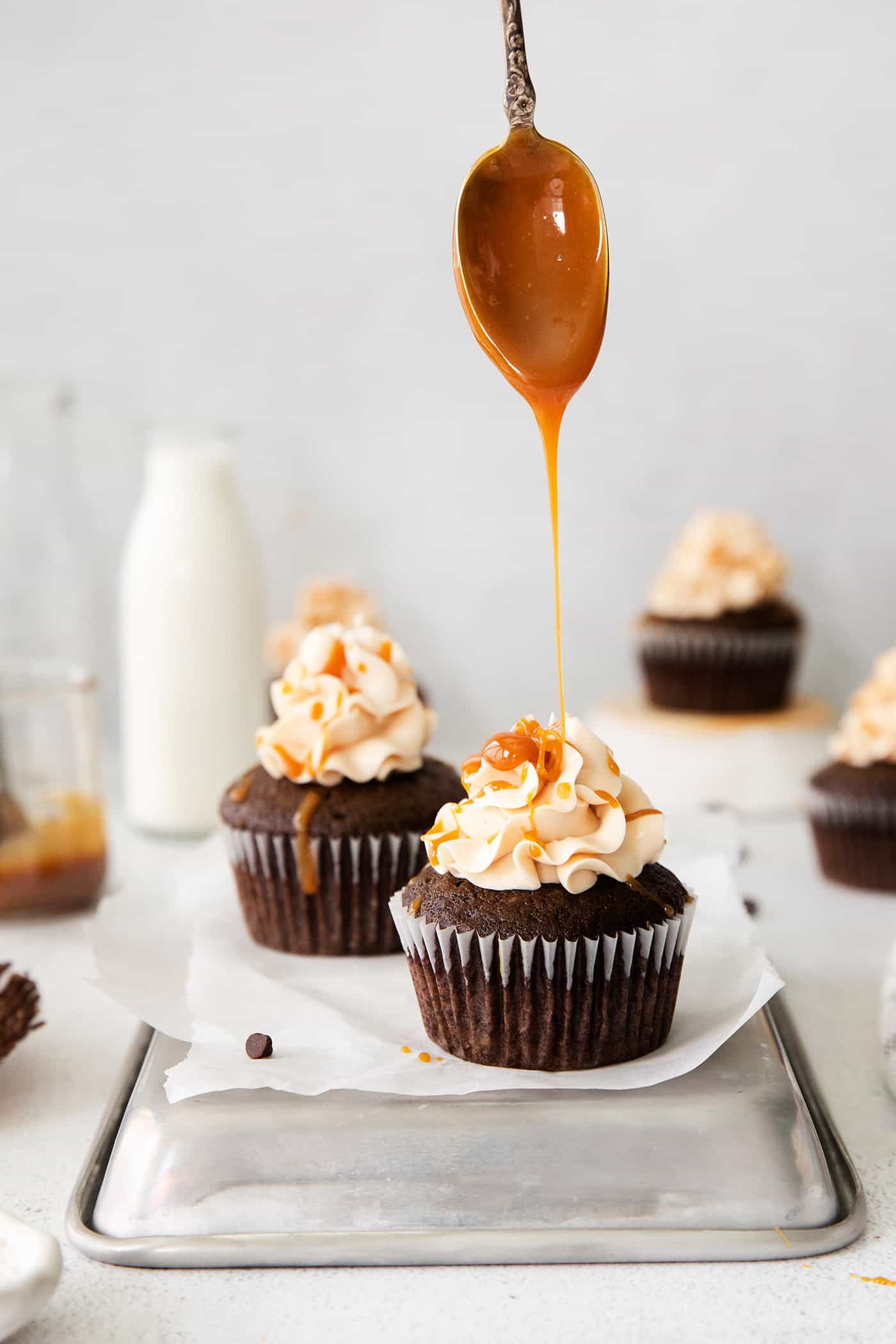 a spoon drizzling caramel sauce over chocolate cupcakes with frosting