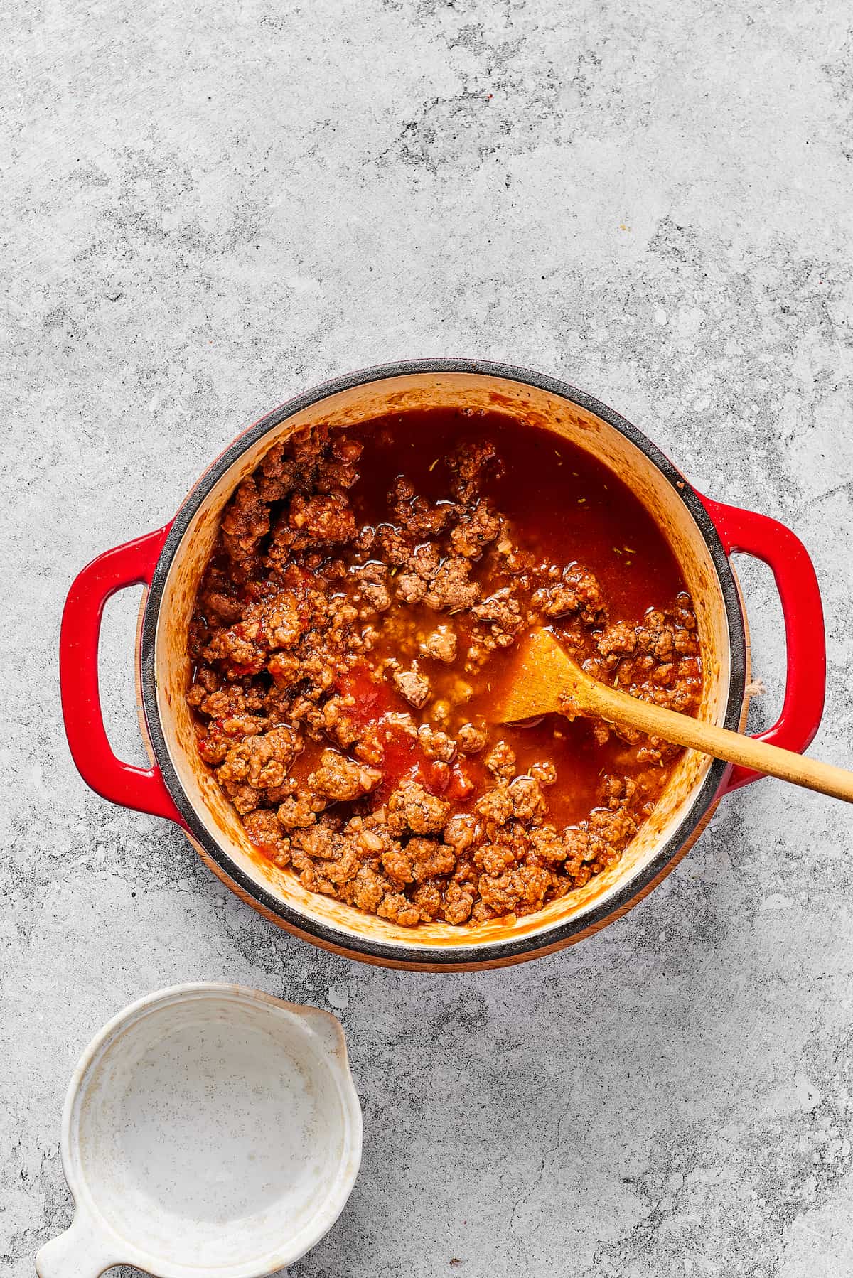 A wooden spoon stirring tomato sauce into ground beef