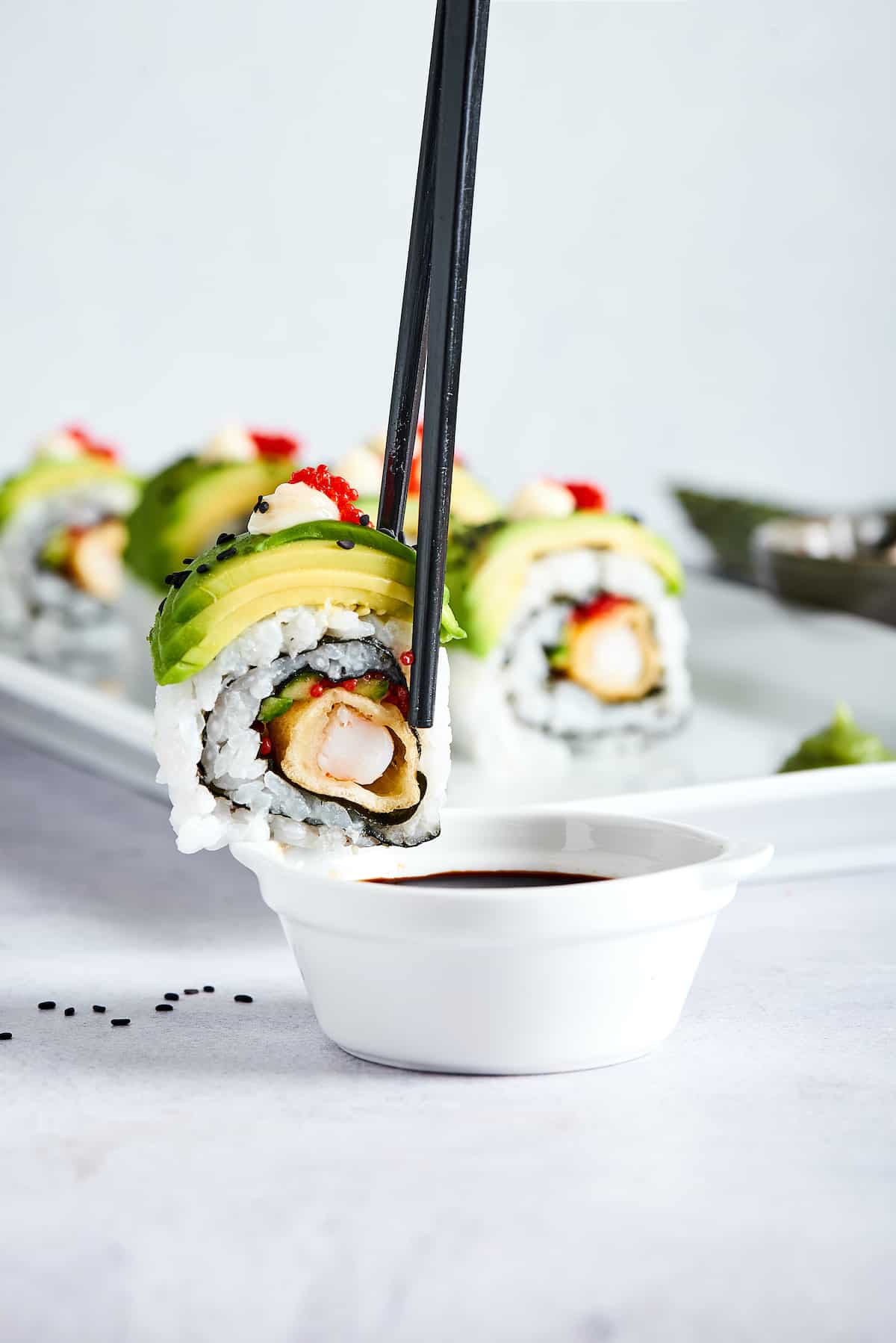 Chop sticks with a piece of dragon roll over a dish of soy sauce.