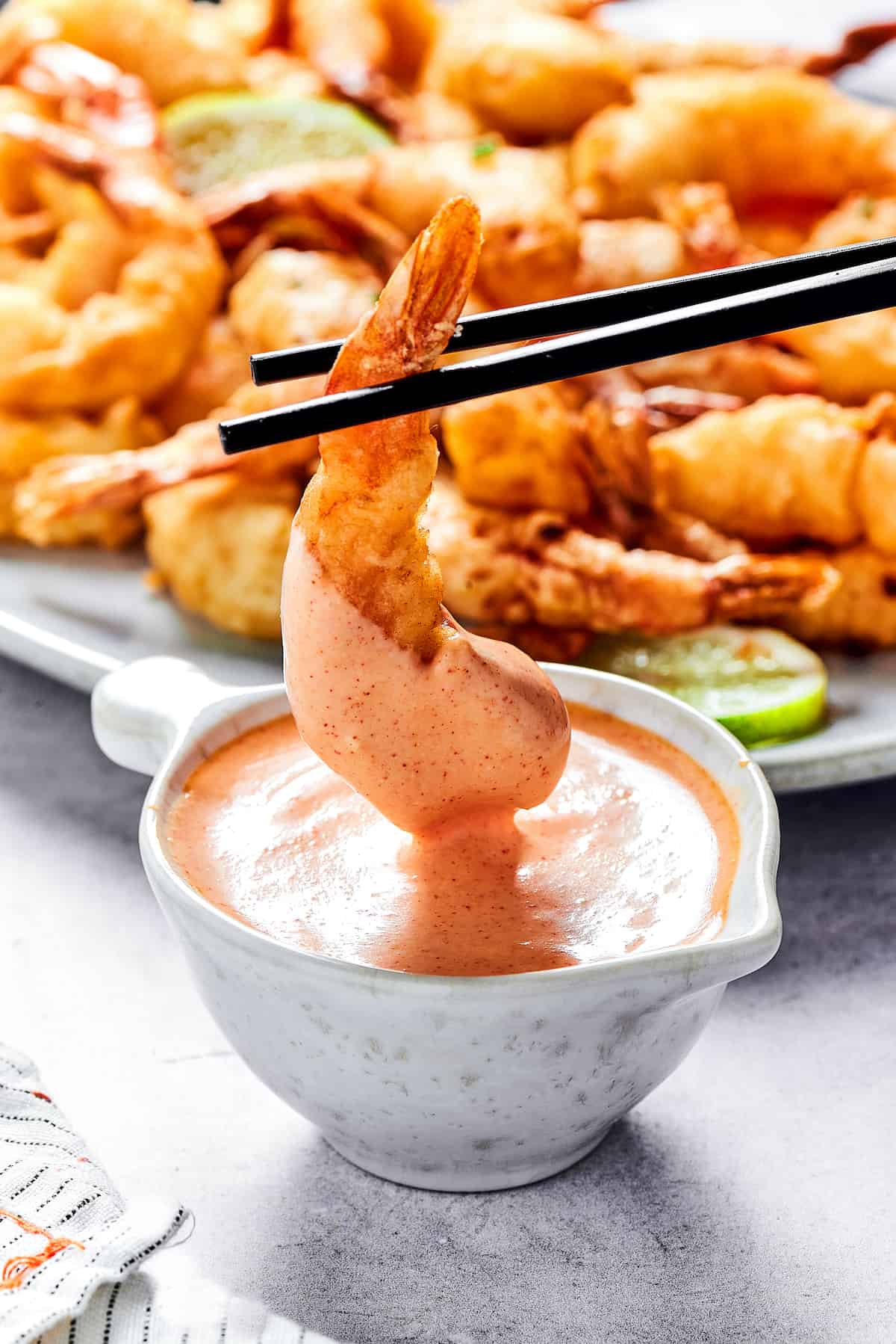 Chopsticks holding a fried shrimp in sauce