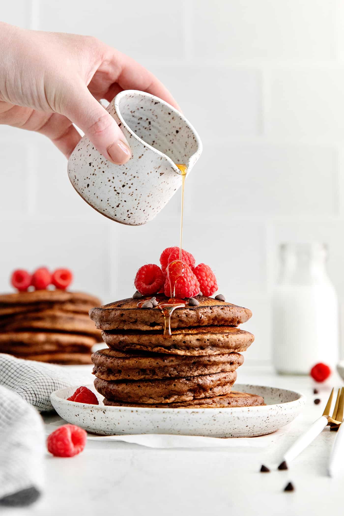 A hand pouring syrup over a stack of chocolate pancakes