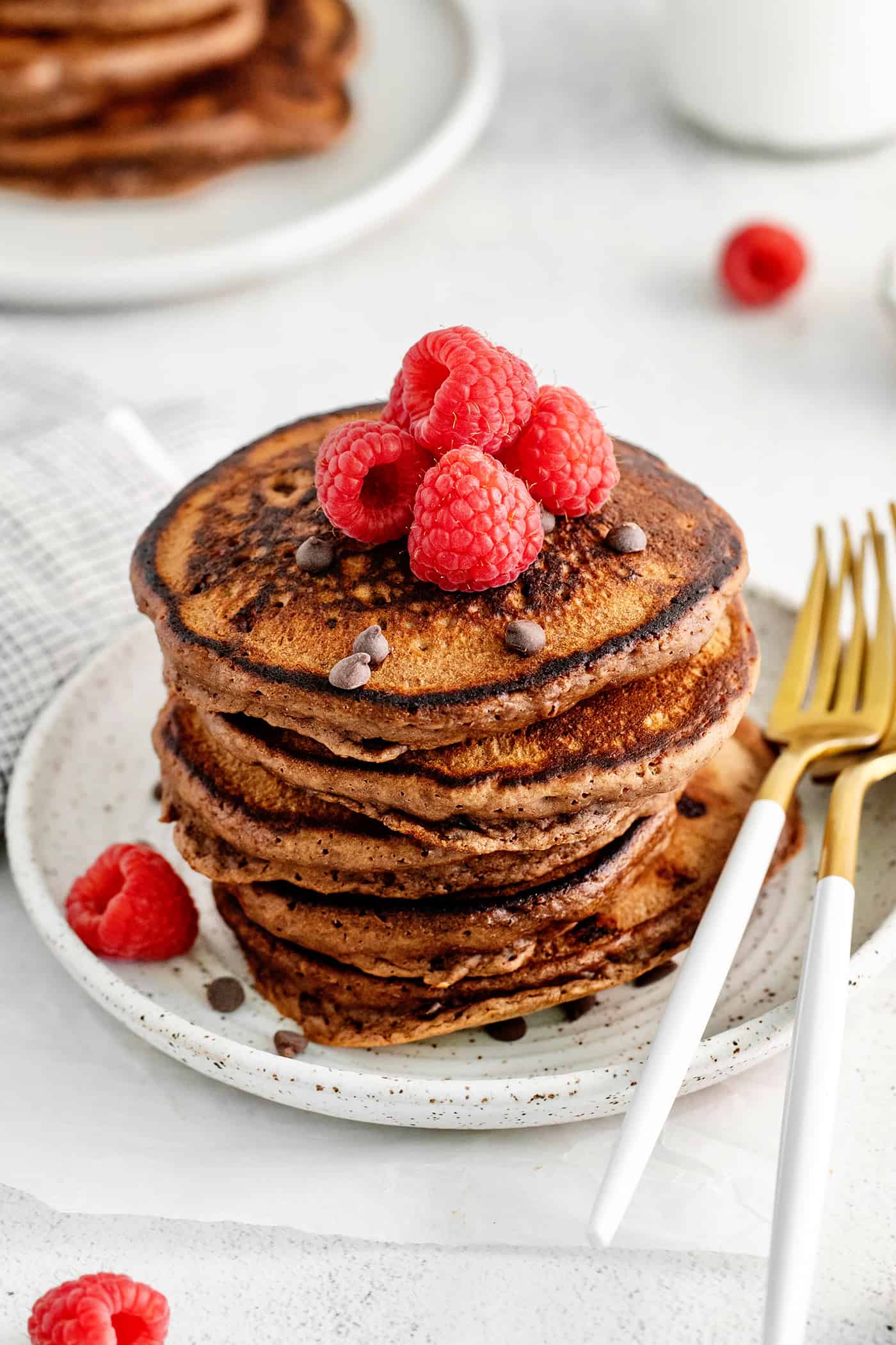 A tall stack of chocolate pancakes topped with raspberries