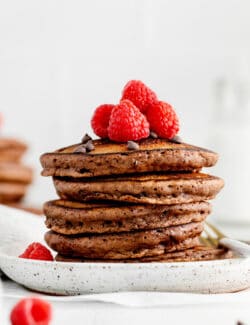 A stack of chocolate pancakes topped with raspberries on a white plate