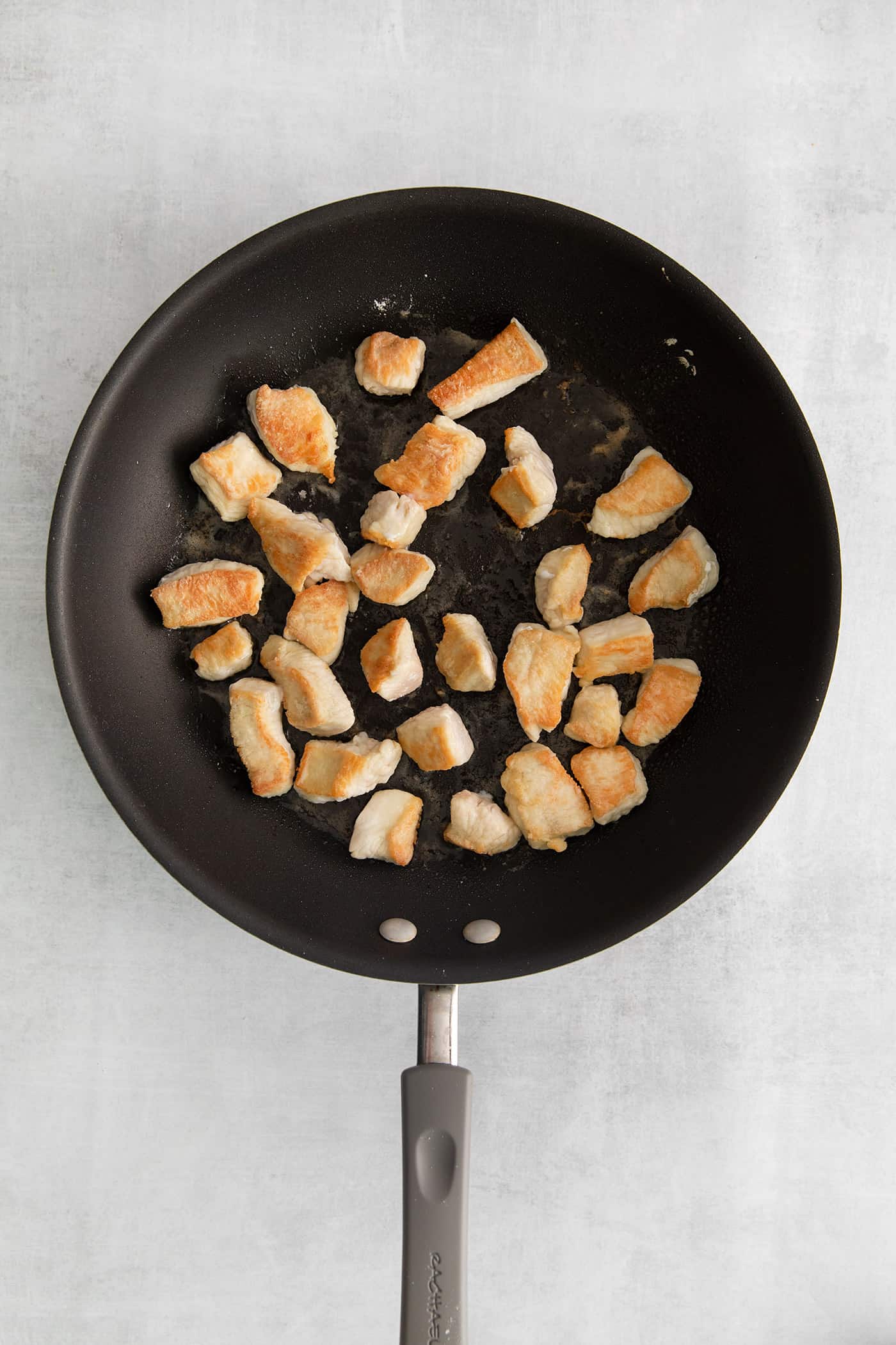 Pieces of seared chicken in a skillet