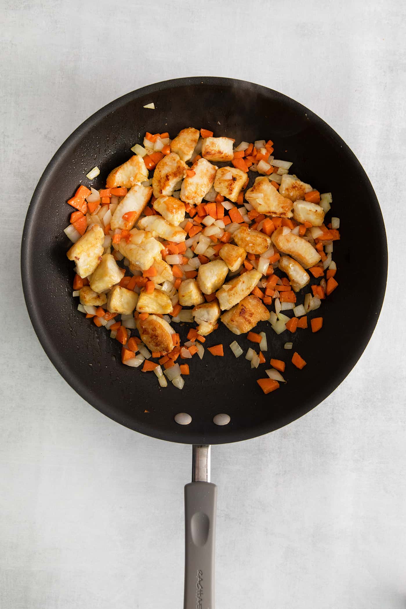 Overhead view of chicken pieces, carrot, and onion in a skillet