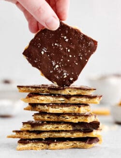 A hand holding a piece of Ritz toffee on a stack of other pieces