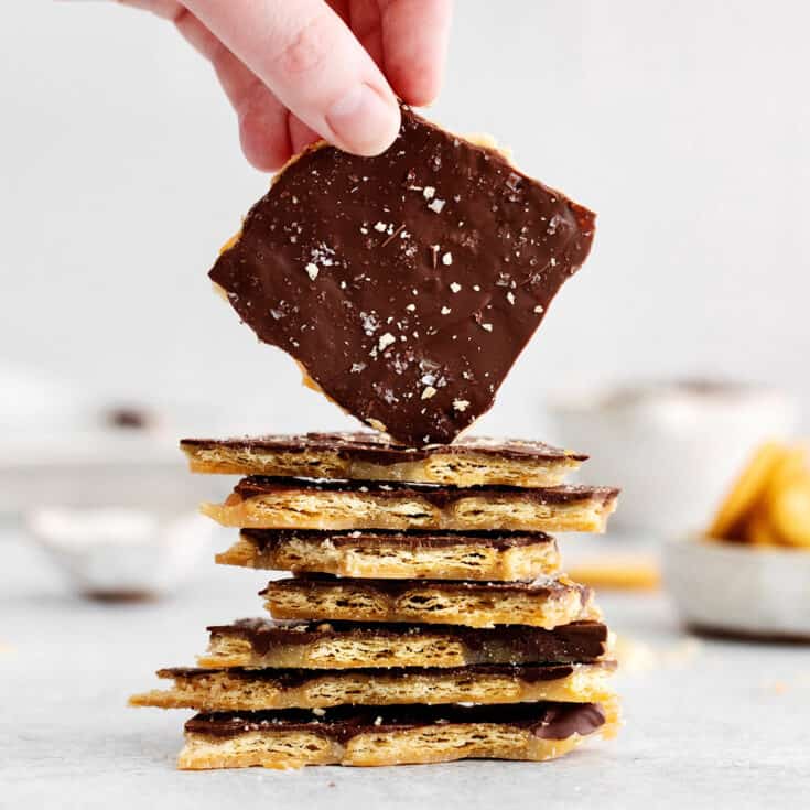A hand holding a piece of Ritz toffee on a stack of other pieces