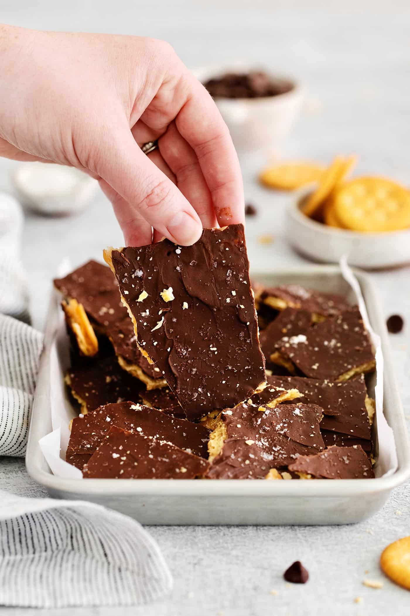 A hand holding a piece of Ritz toffee above a pan of toffee