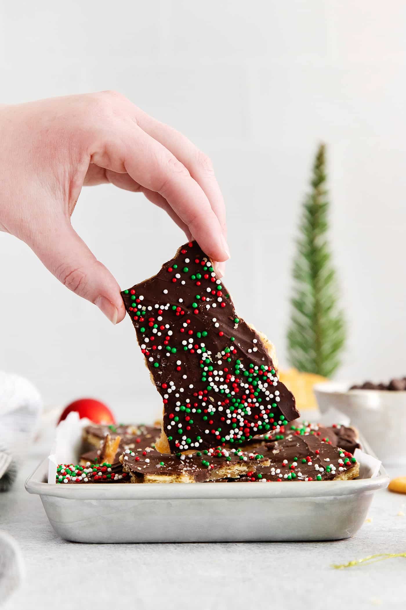 A hand holding a piece of Christmas crack above a bowl of more pieces