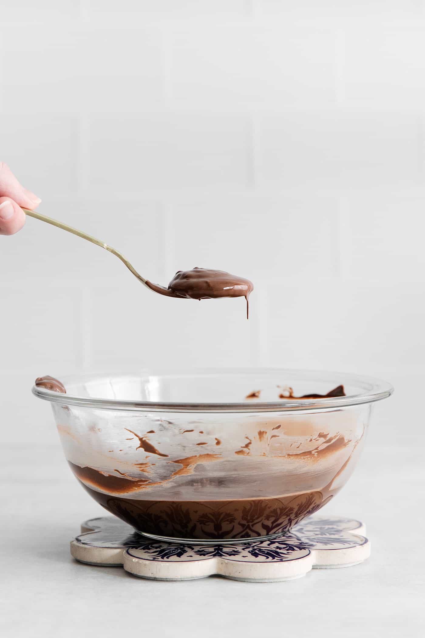 A spoon holding a chocolate dipped ritz cracker over a bowl of chocolate