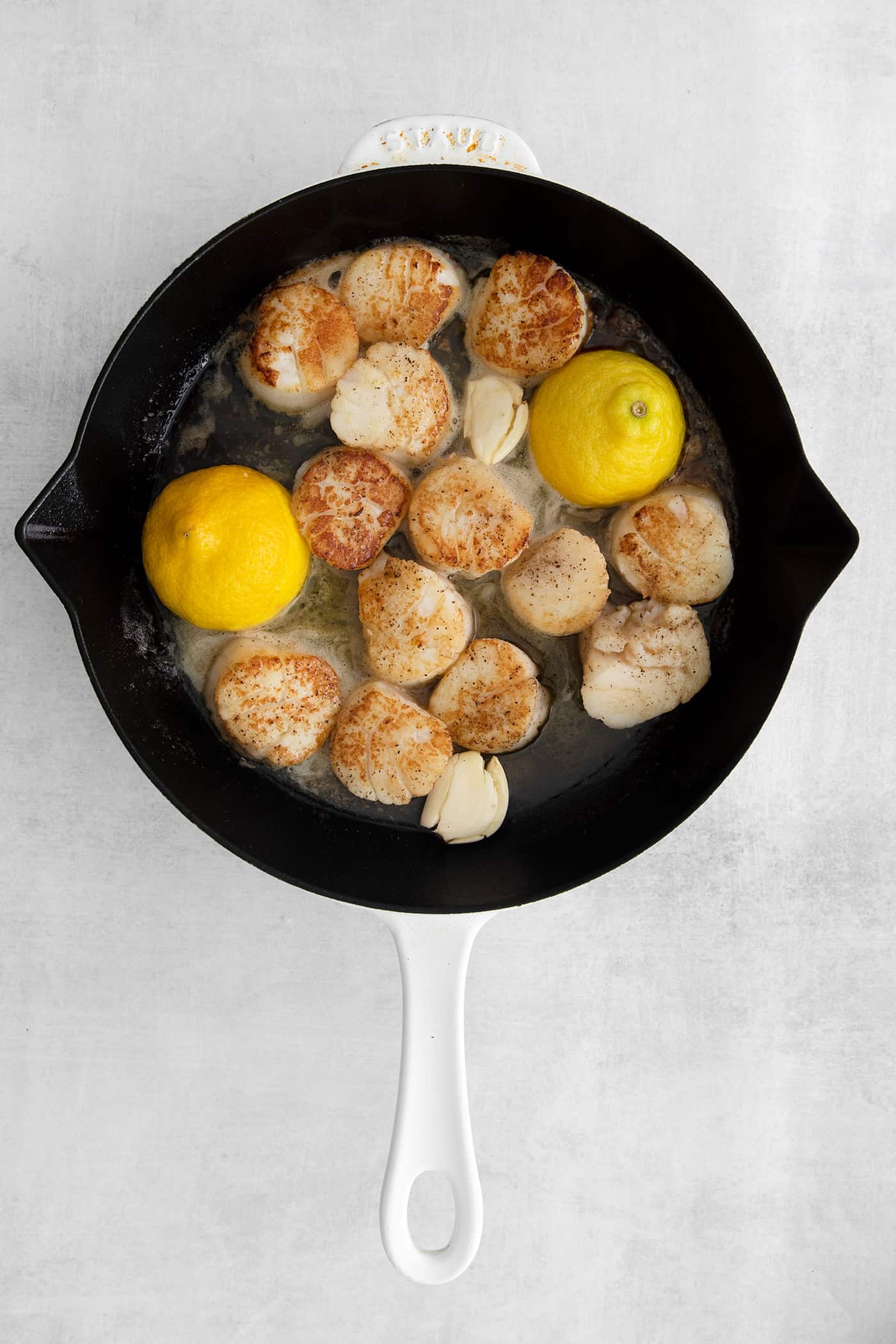 Overhead view of seared scallops with lemon in a skillet