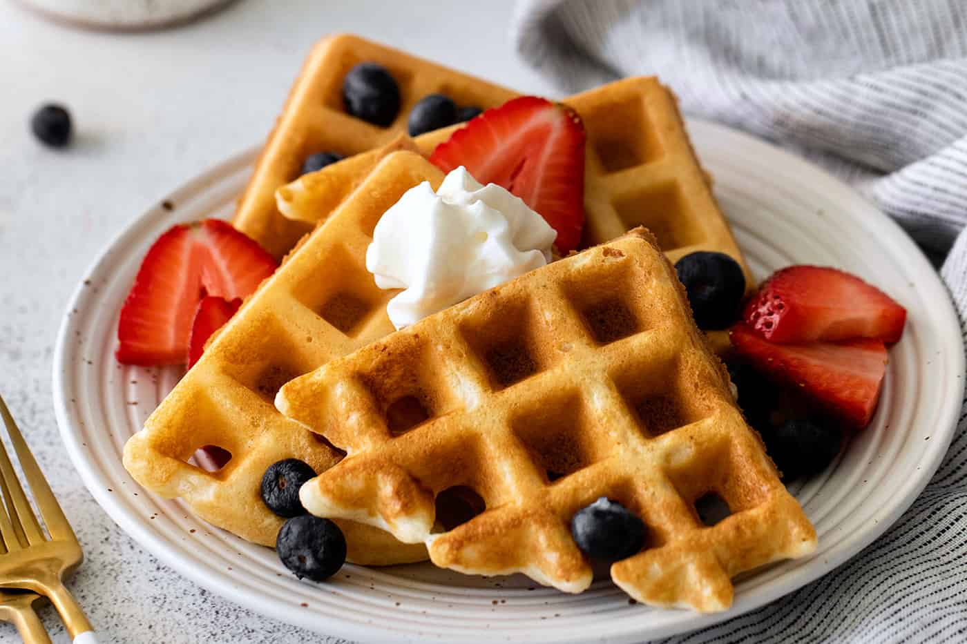 overnight waffles made with yeast, on a plate with berries and whipped cream