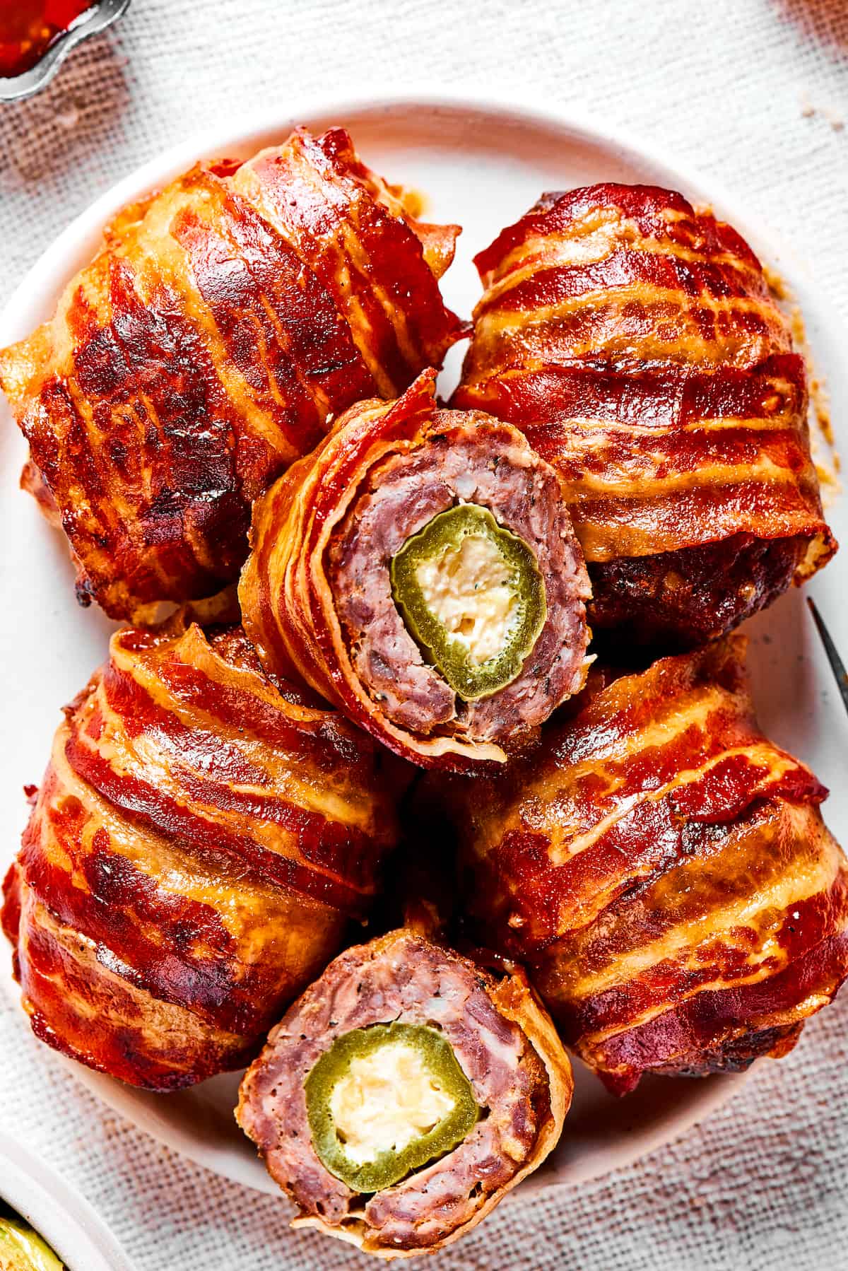 If you love jalapeno poppers, you are going to LOVE these Armadillo Eggs - cheese-stuffed jalapenos wrapped in bacon and sausage. Yum! Close up of armadillo eggs on a white plate, with one cut in half