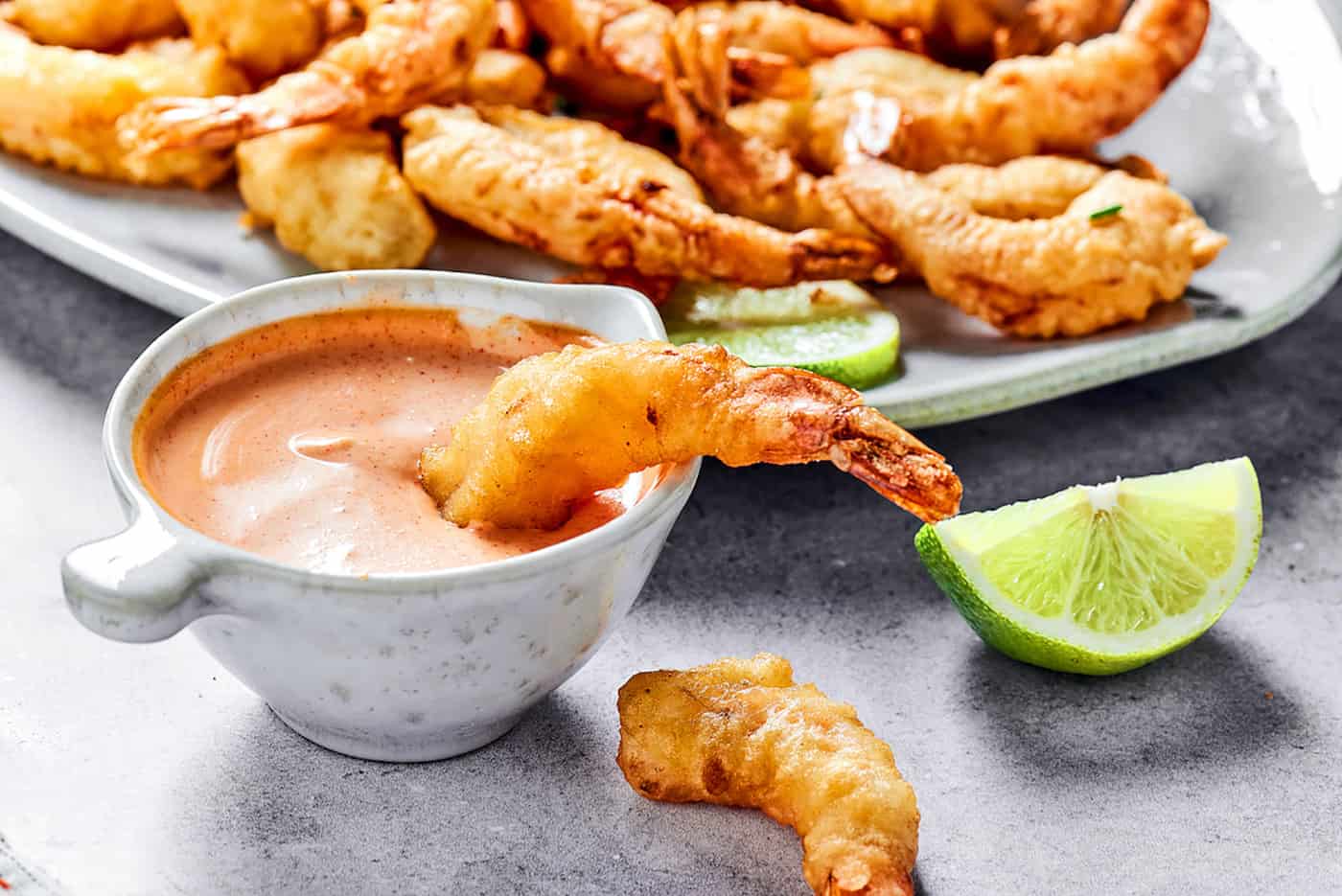 dipping shrimp tempura into a small bowl of creamy sauce