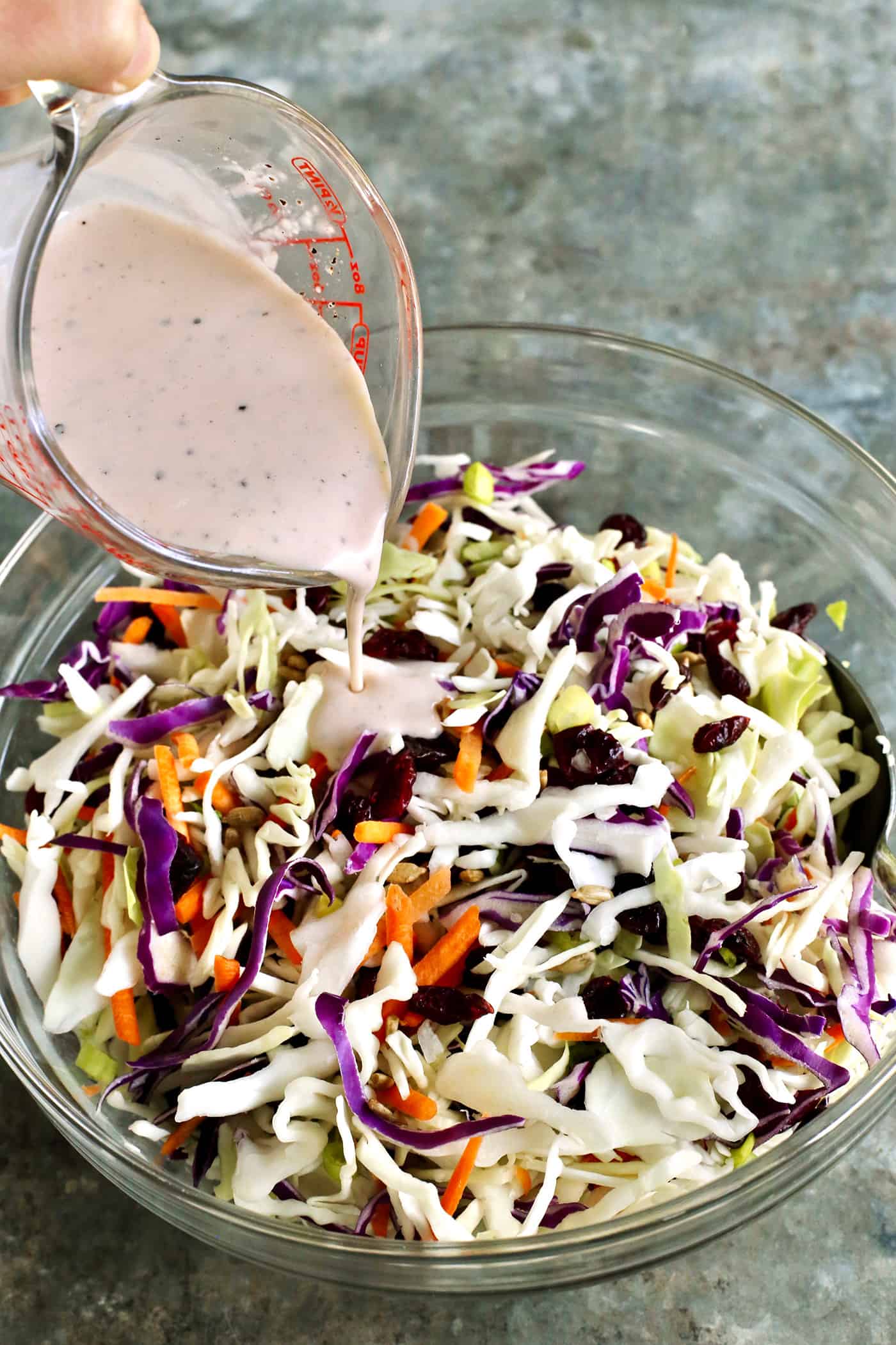 Dressing being poured over a bowl of coleslaw