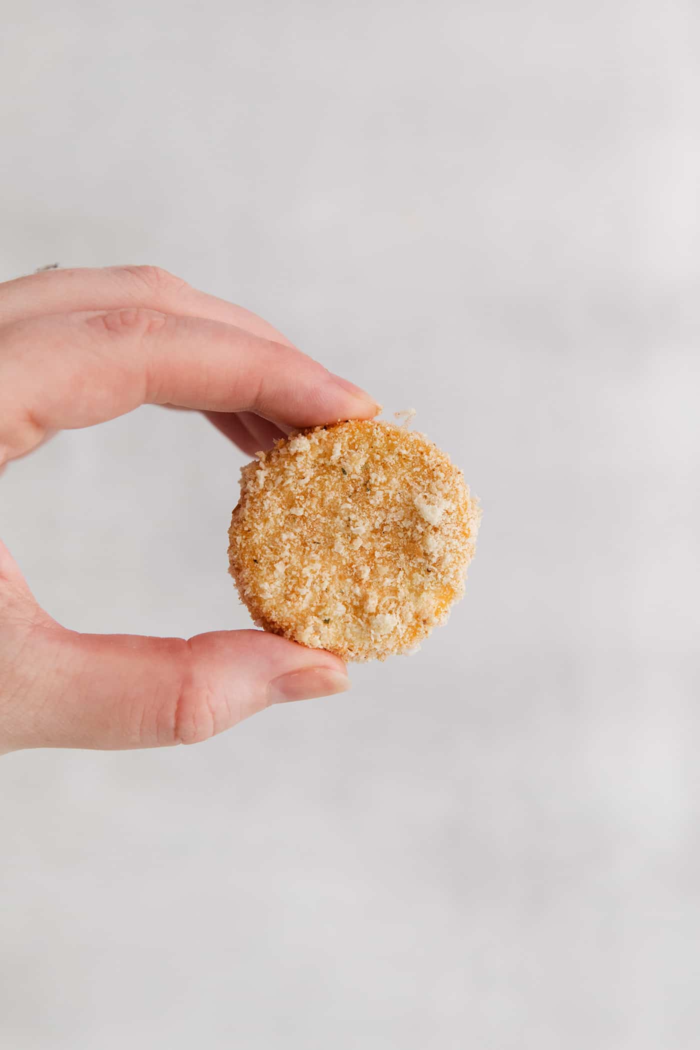 A hand holding a squash rounded coated in bread crumbs