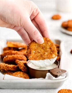 A hand holding a squash round dipped into ranch