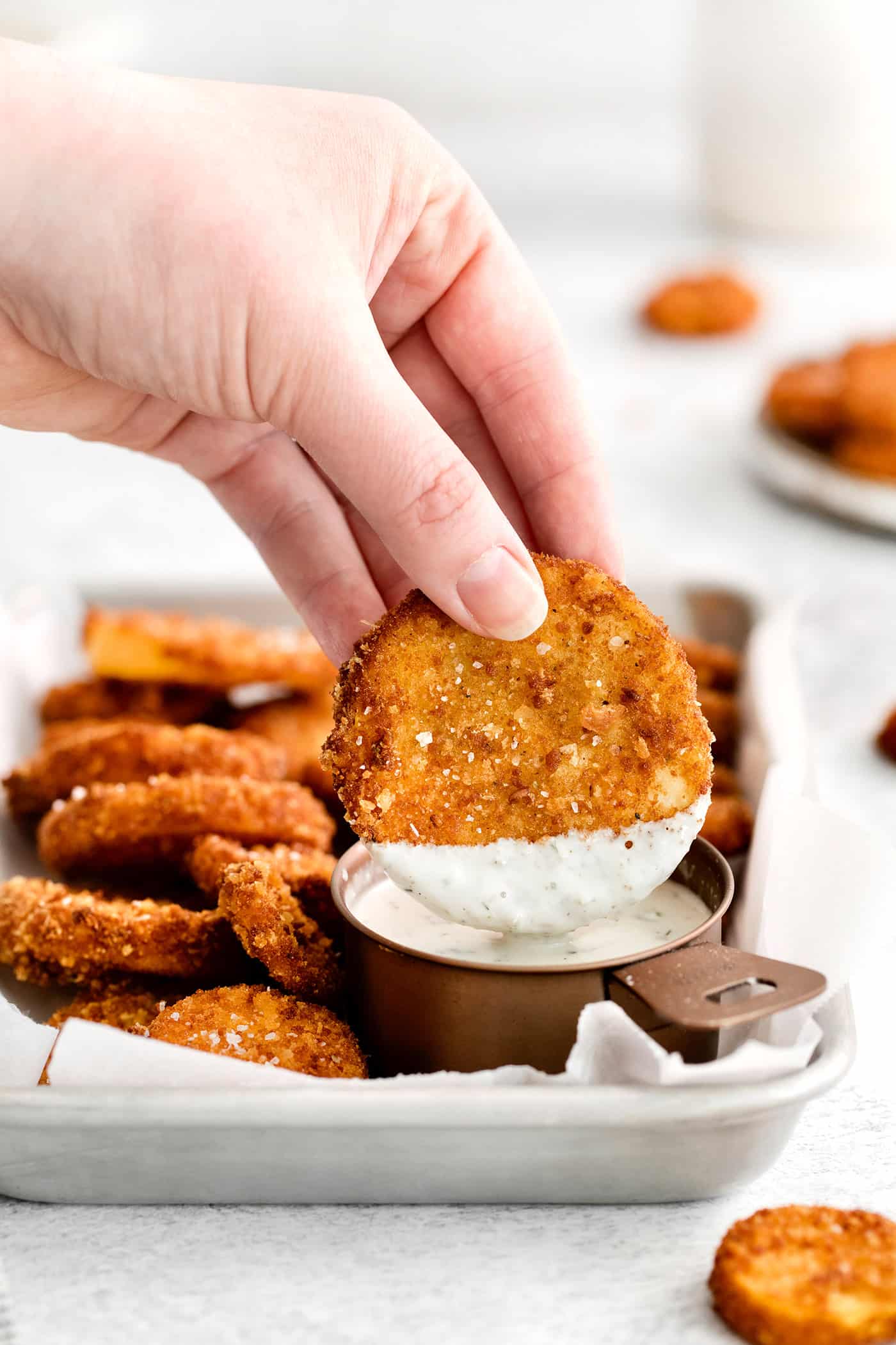 A hand holding a squash round dipped into ranch