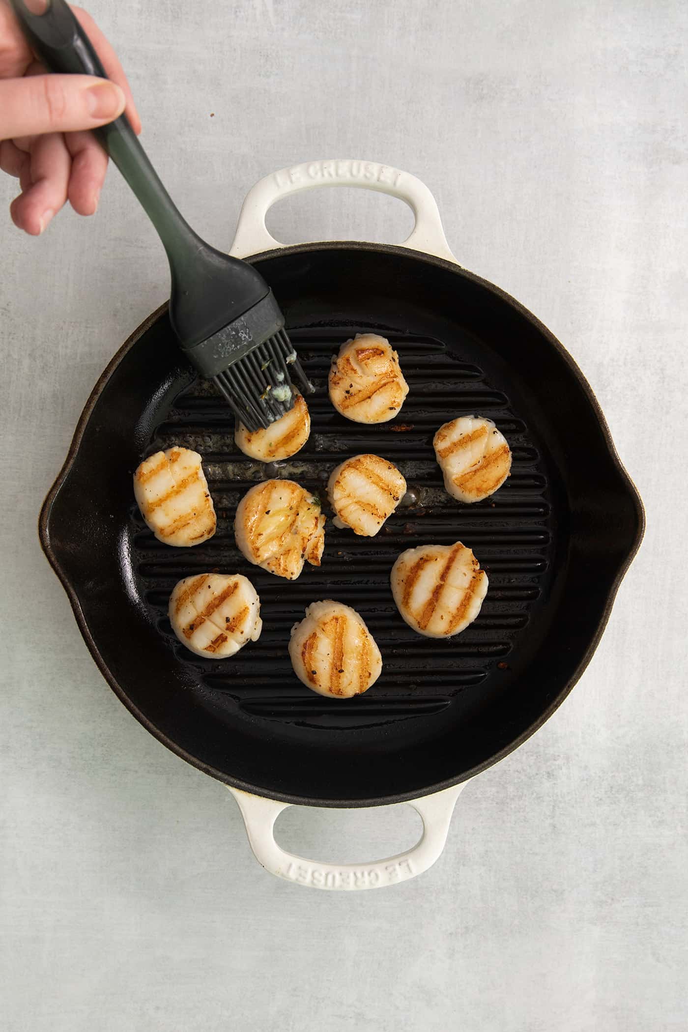 Garlic butter being brushed on grilled scallops