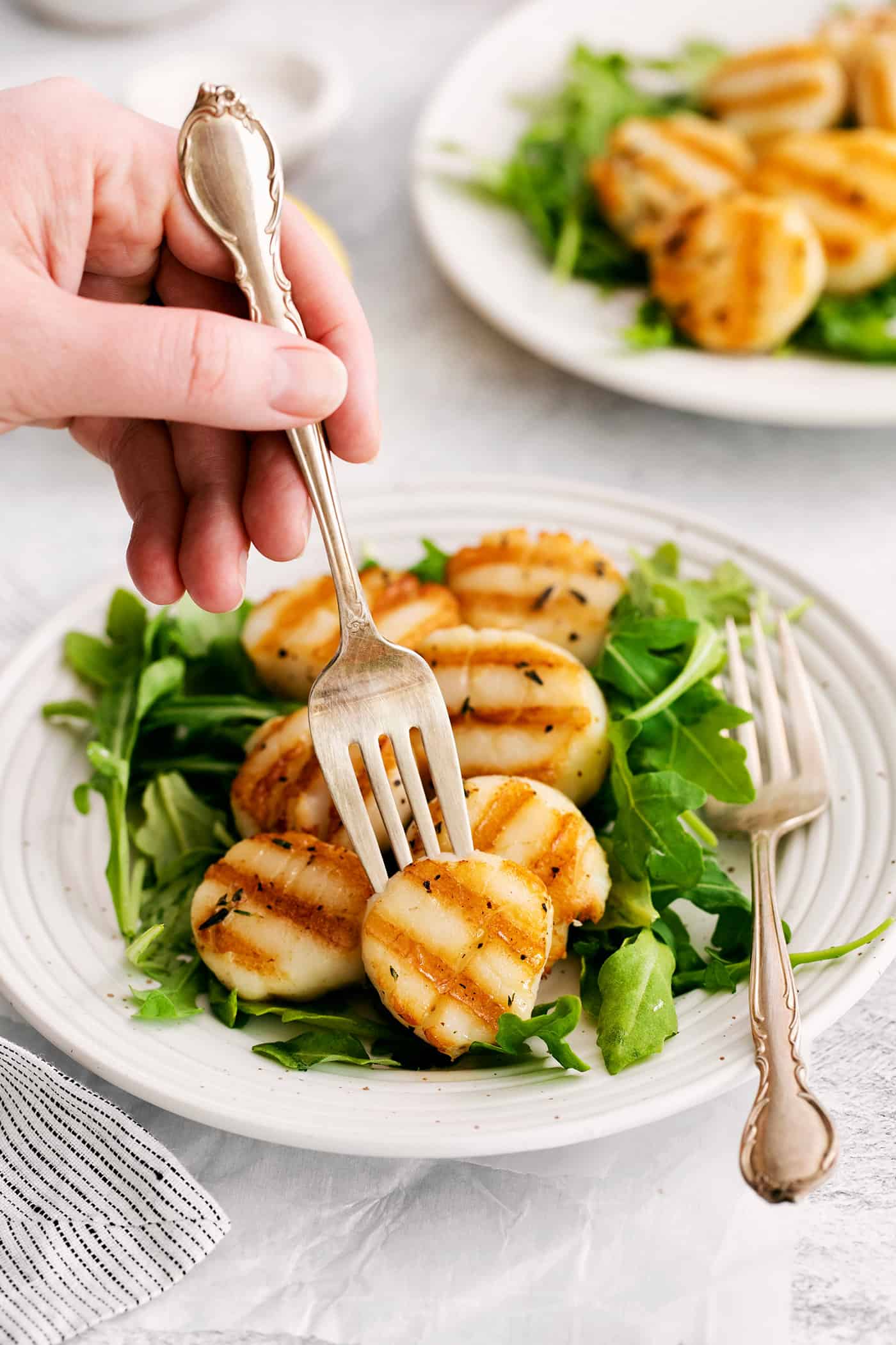 A fork in a grilled scallop over a bed of greens