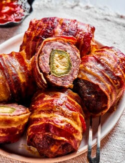 a plate of baked armadillo eggs, with one cut open to reveal the stuffed jalapeno inside