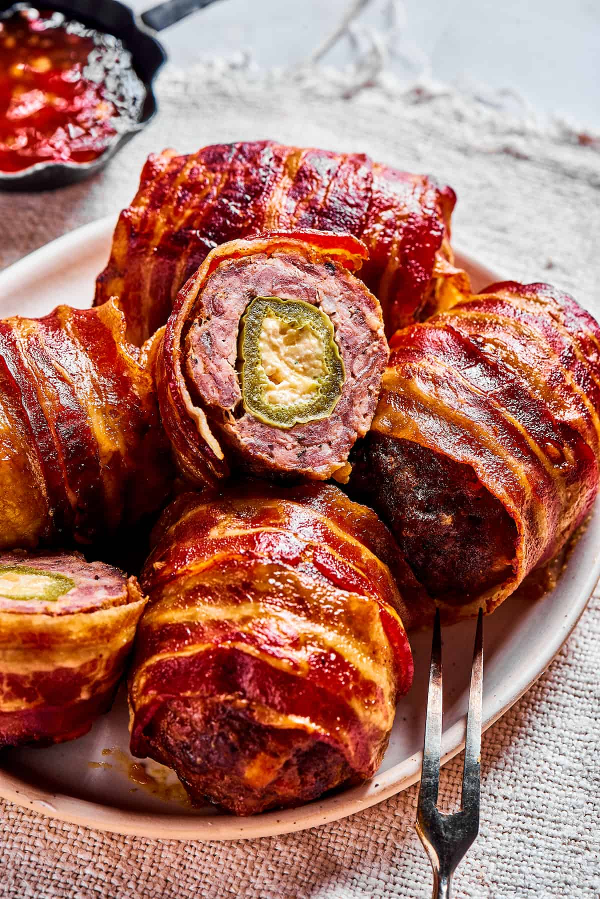 a plate of baked armadillo eggs, with one cut open to reveal the stuffed jalapeno inside