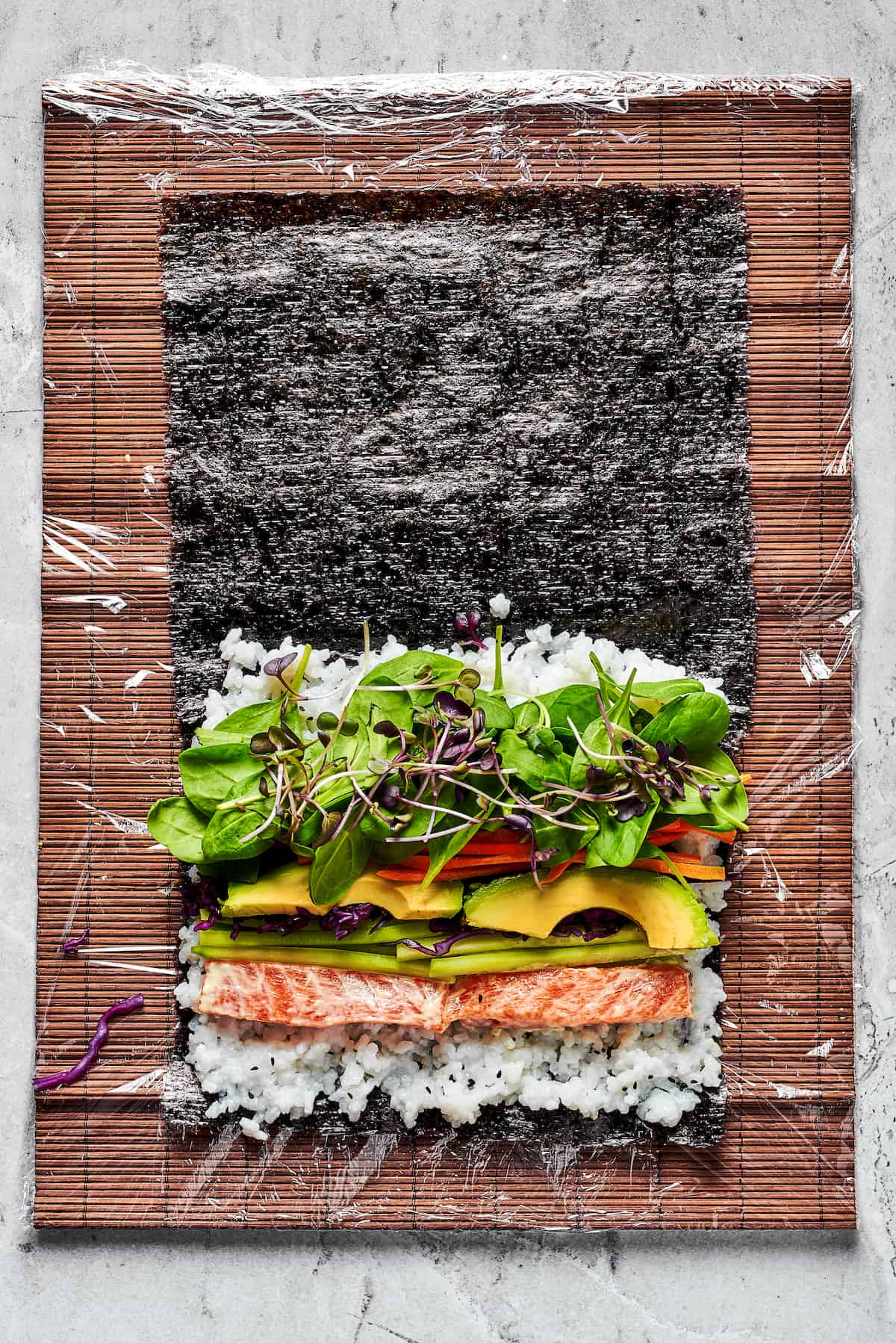 Overhead view of a salmon, rice, and veggies on nori sheets