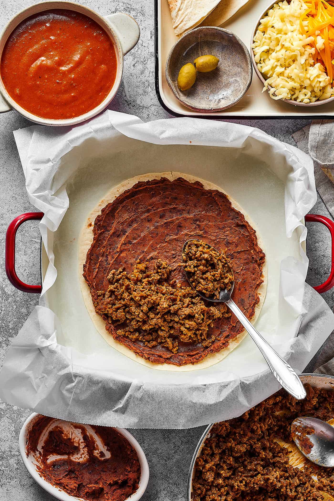 adding refried beans and taco meat to a tortilla