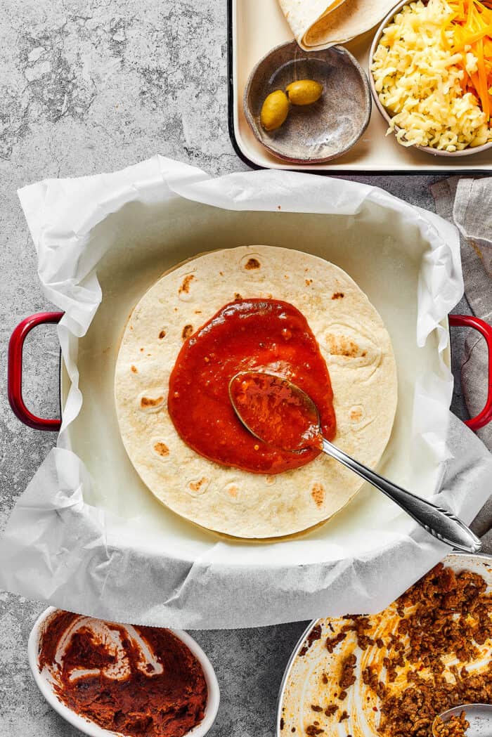 adding enchilada sauce to the top of a tortilla