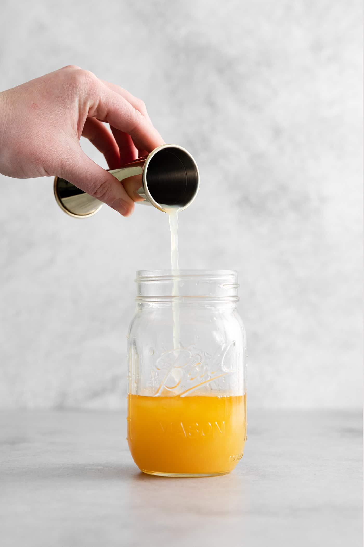 A hand pouring bourbon into a mason jar